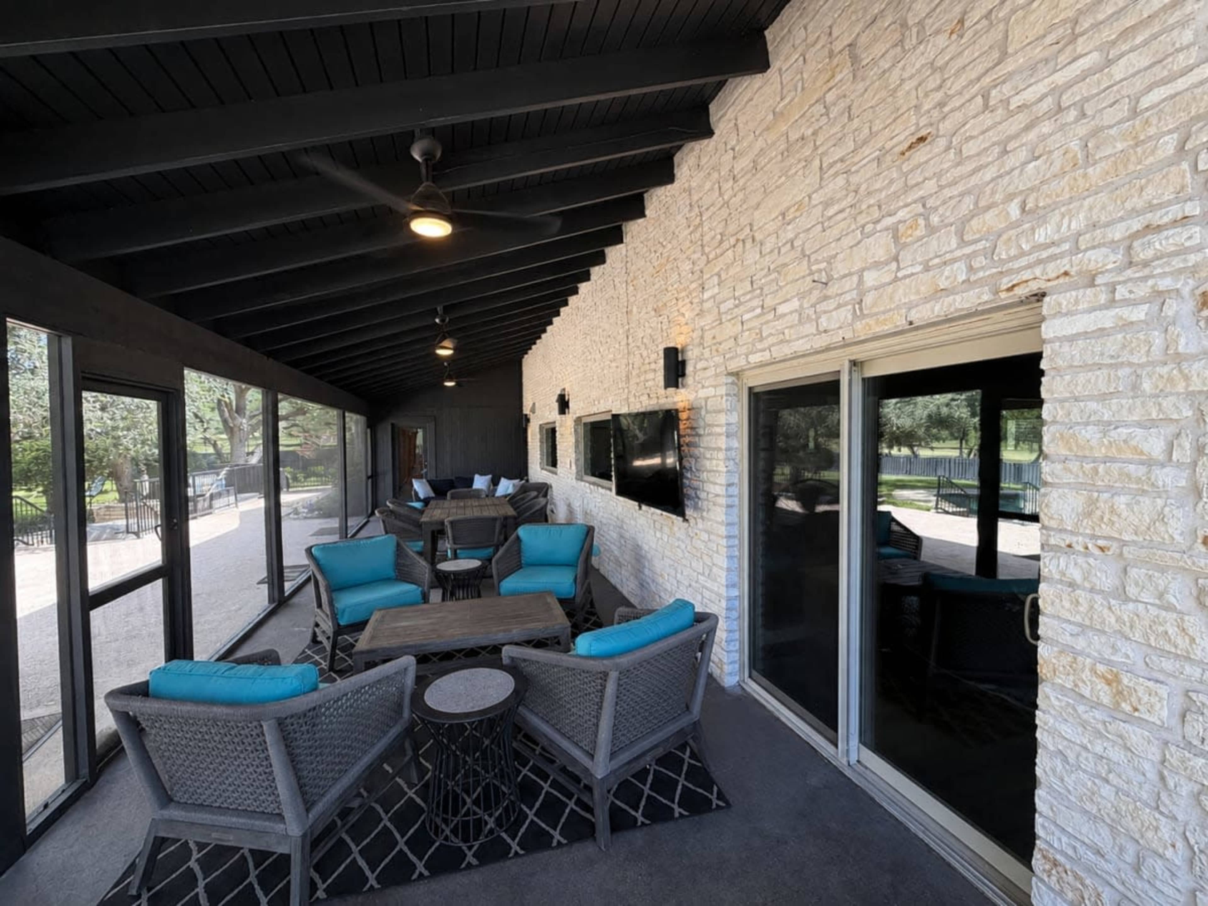 The image shows a covered outdoor lounge area featuring stone walls, modern seating with blue cushions, and large sliding glass doors leading to a patio.