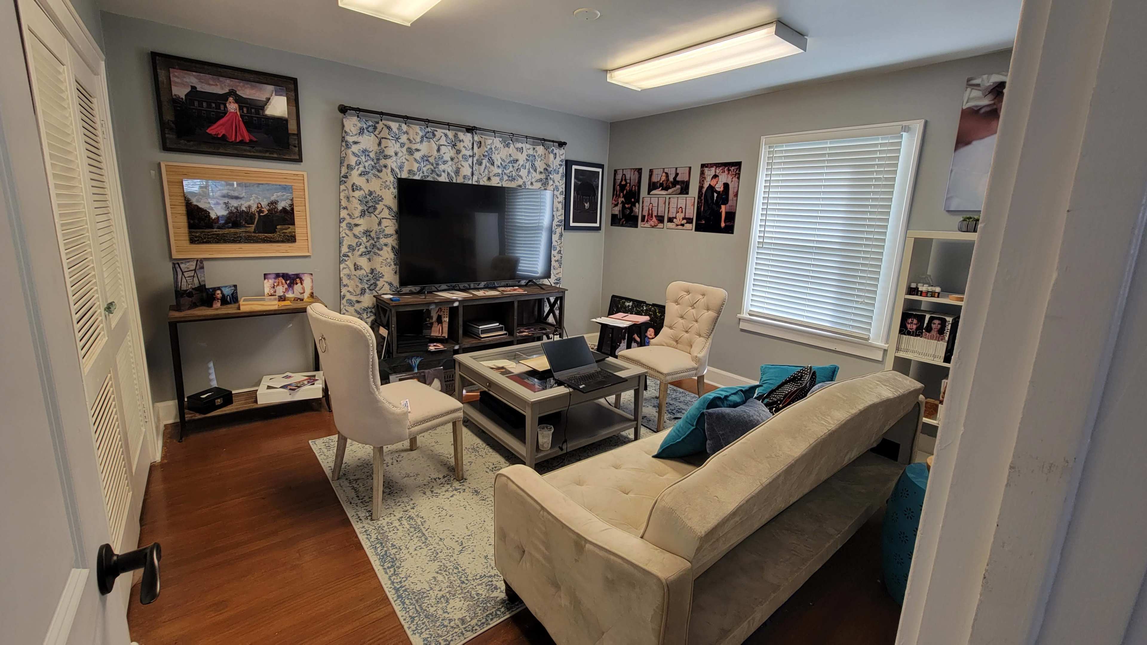 A neatly arranged living room with a sofa, two chairs, a coffee table, a television, and various framed photographs on the walls.