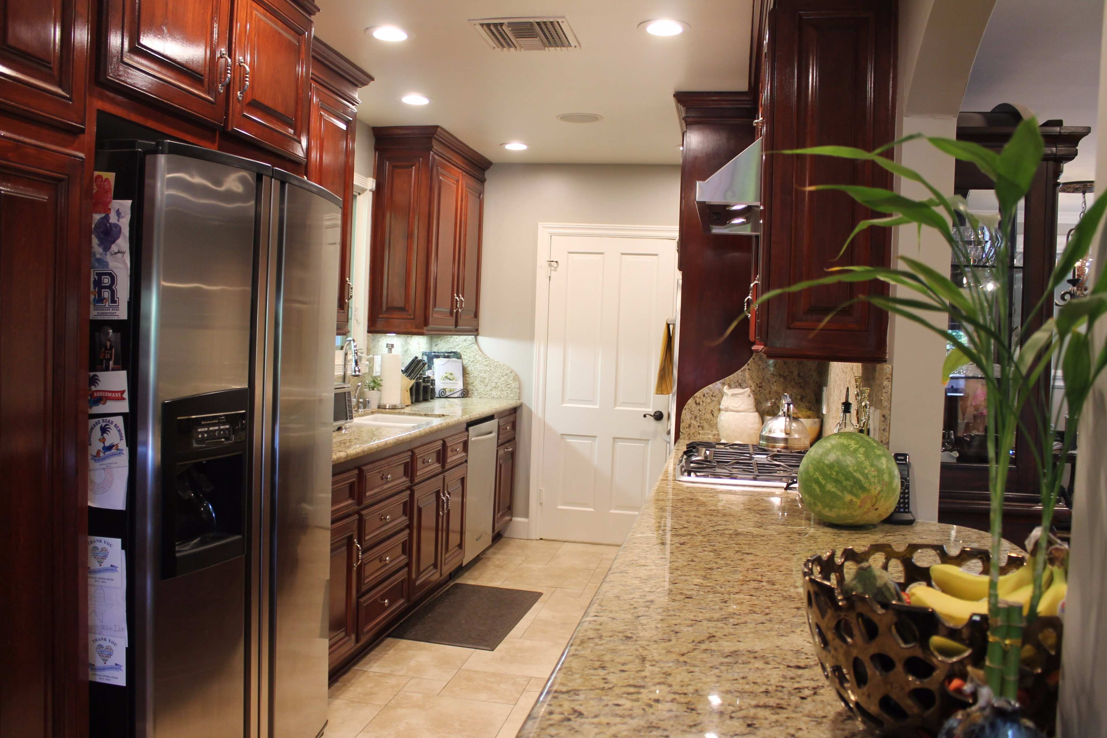 The image shows a modern kitchen with wooden cabinets, stainless steel appliances, and a granite countertop.