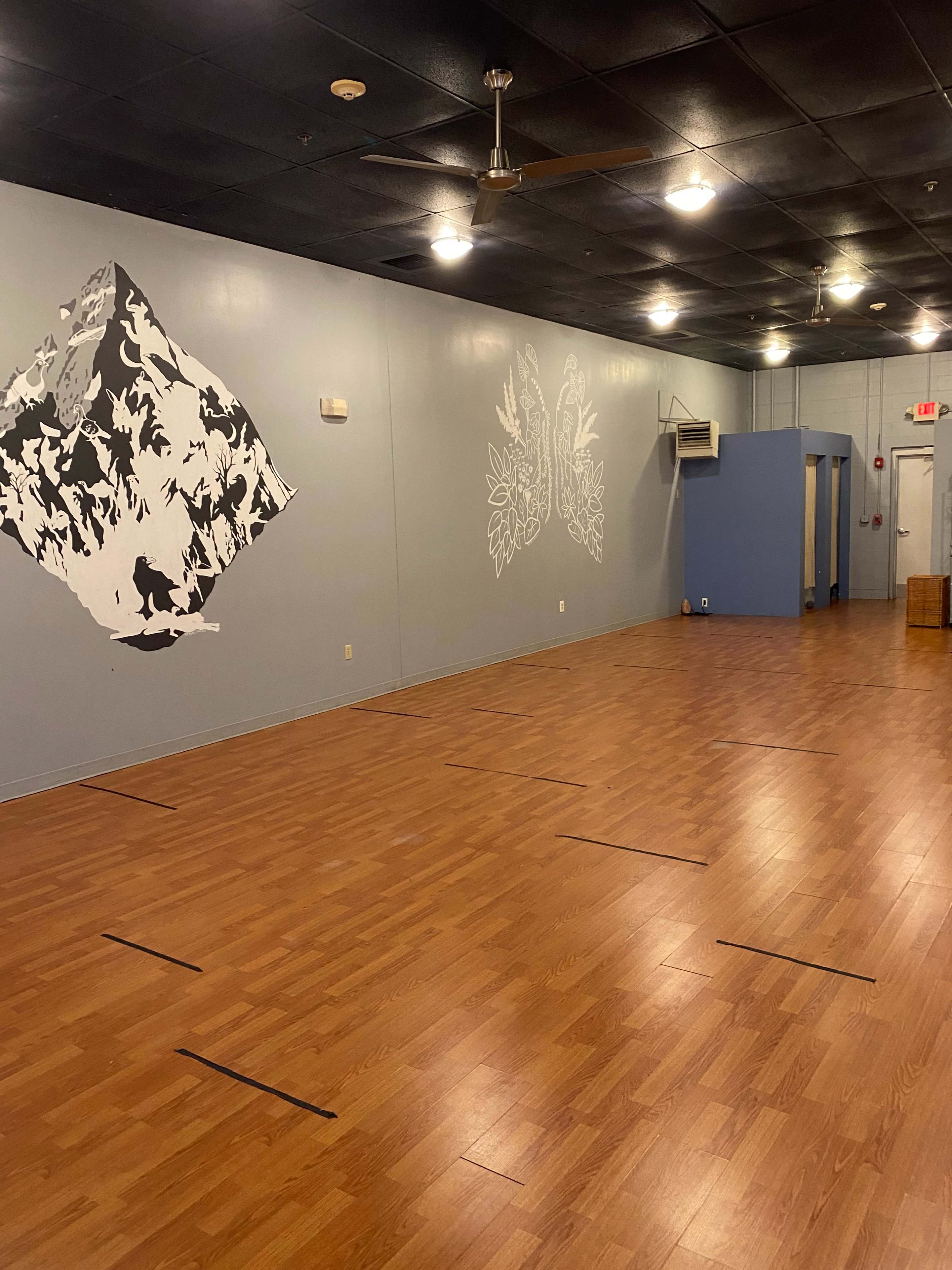 An empty studio space with wooden flooring, light gray walls featuring black and white artwork, and a blue wall section at one end.
