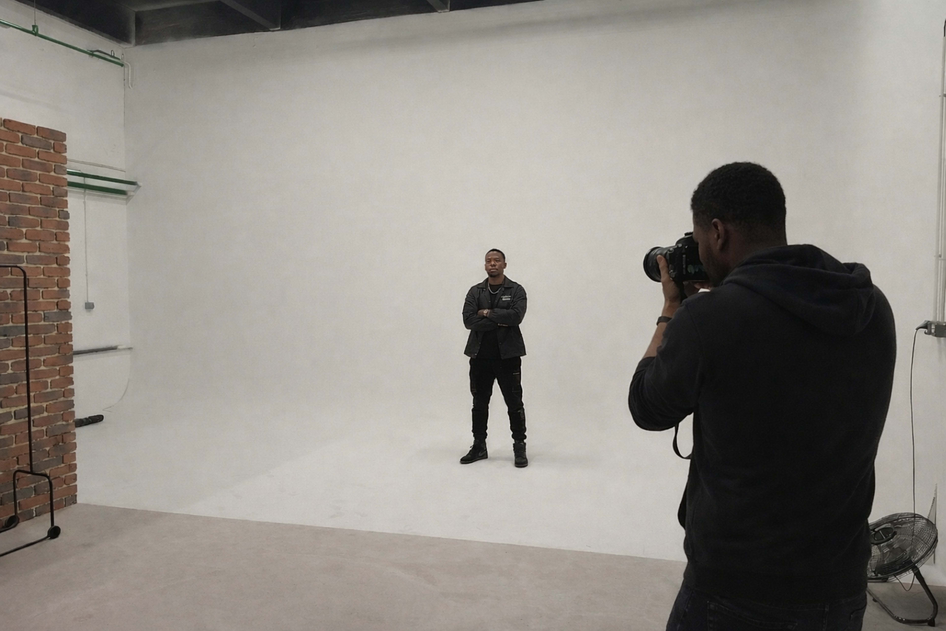 A photographer captures a subject standing confidently in a spacious, minimally furnished studio.