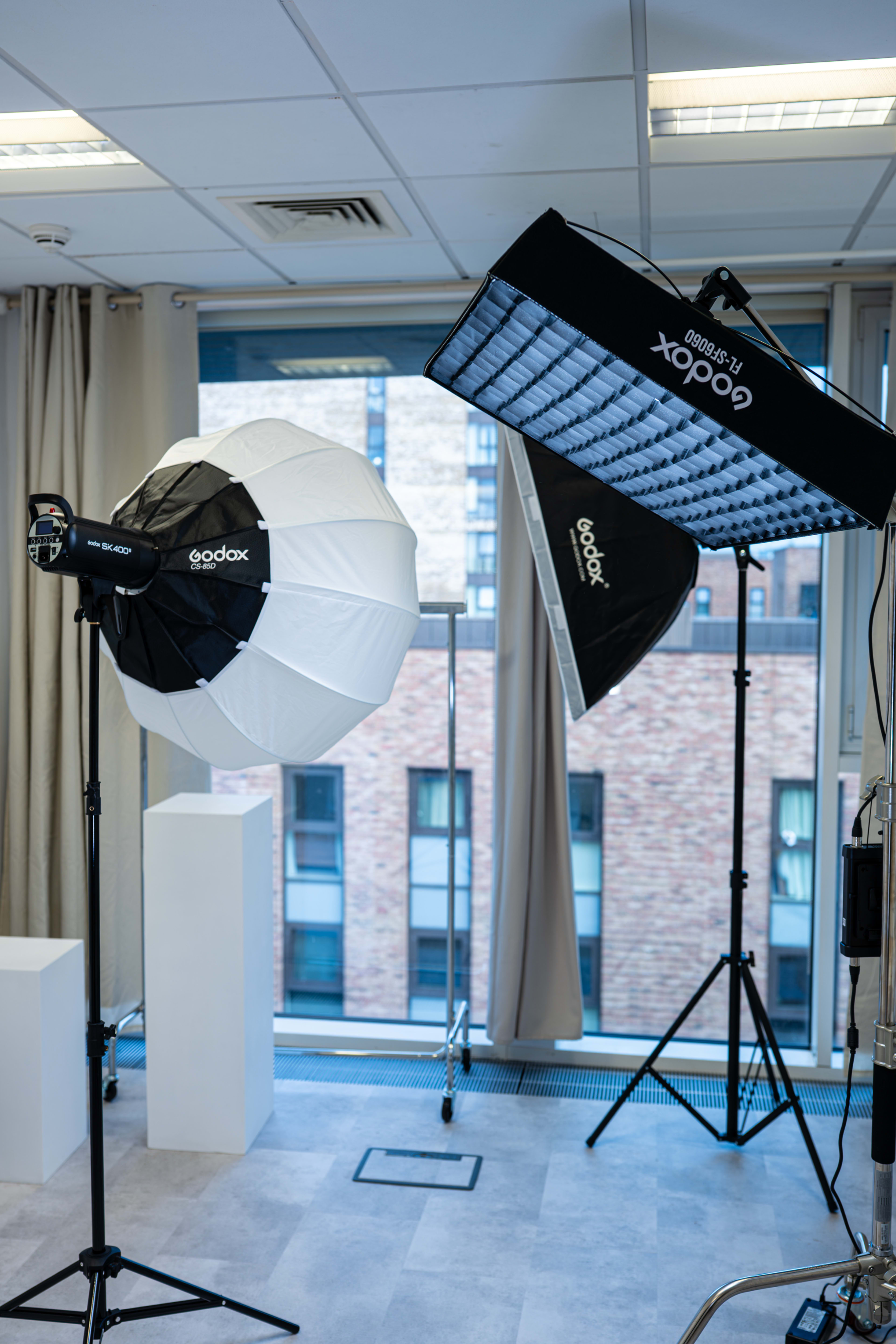 The image shows a well-lit studio setup featuring two softbox lighting equipment pieces, one round and one rectangular, positioned near a window.