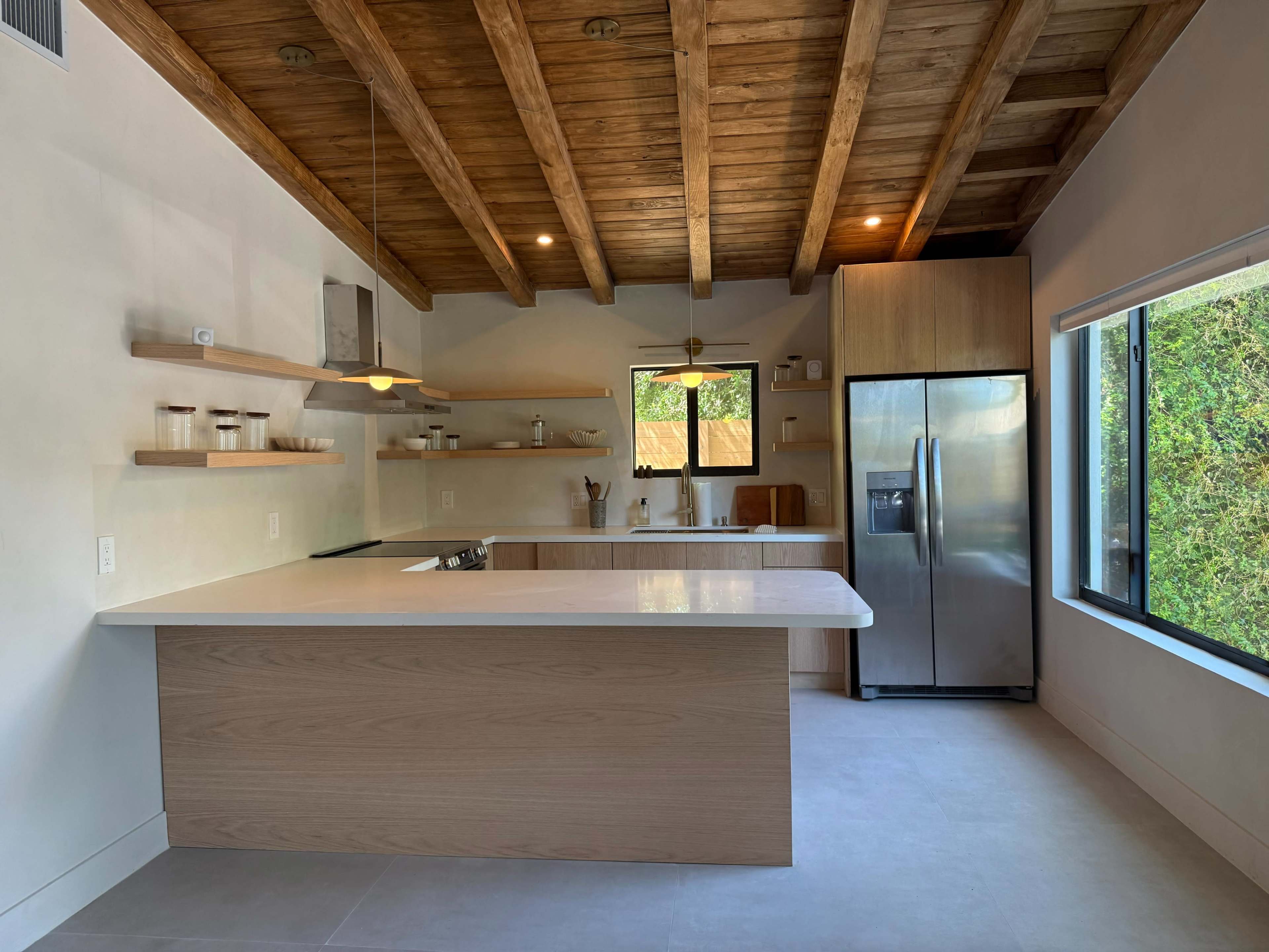 The image shows a modern kitchen featuring wooden beams, an island with a white countertop, and stainless steel appliances.