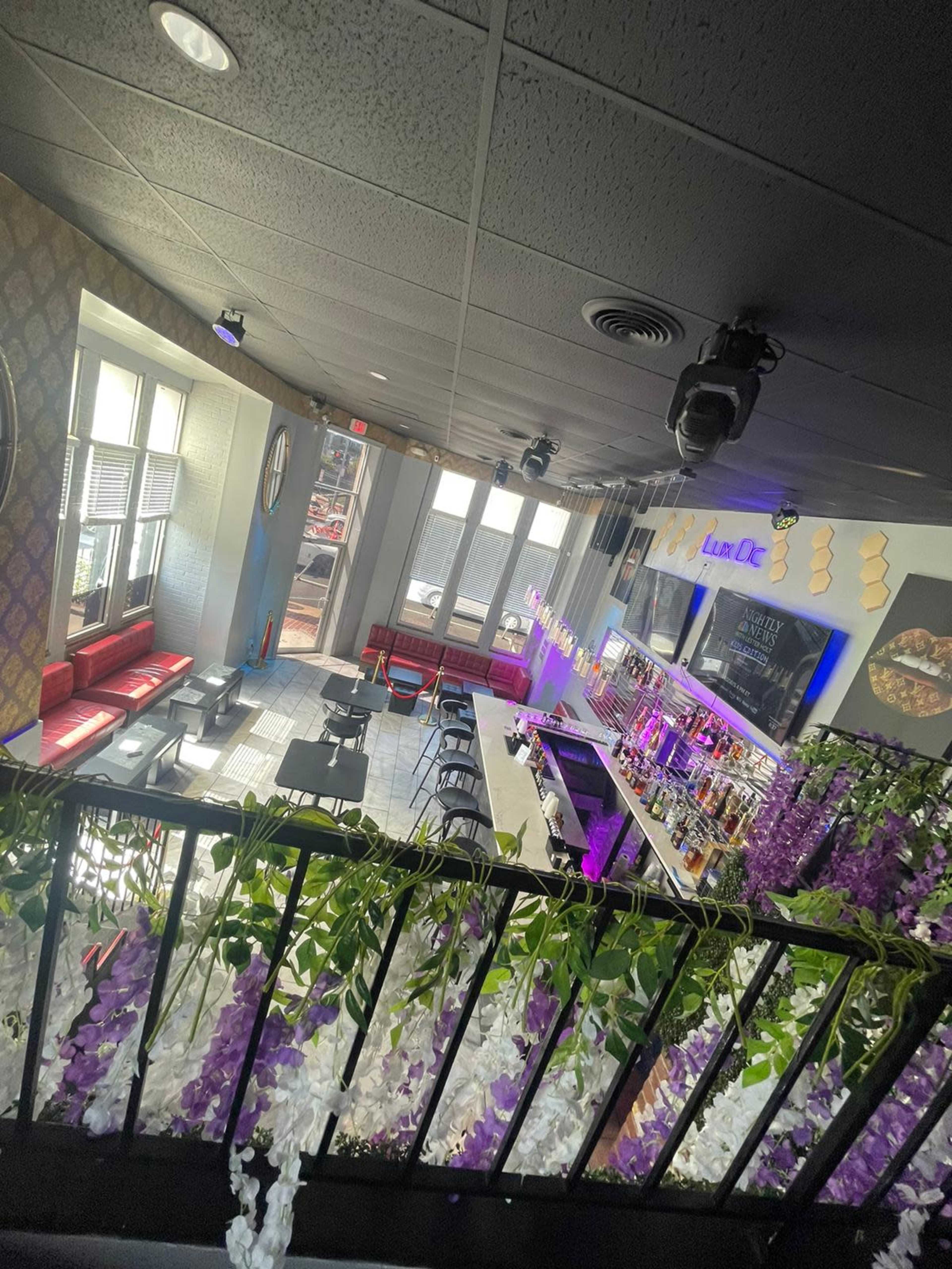 The image shows a brightly lit bar and dining area with seating arranged around a central bar, adorned with decorative flowers.