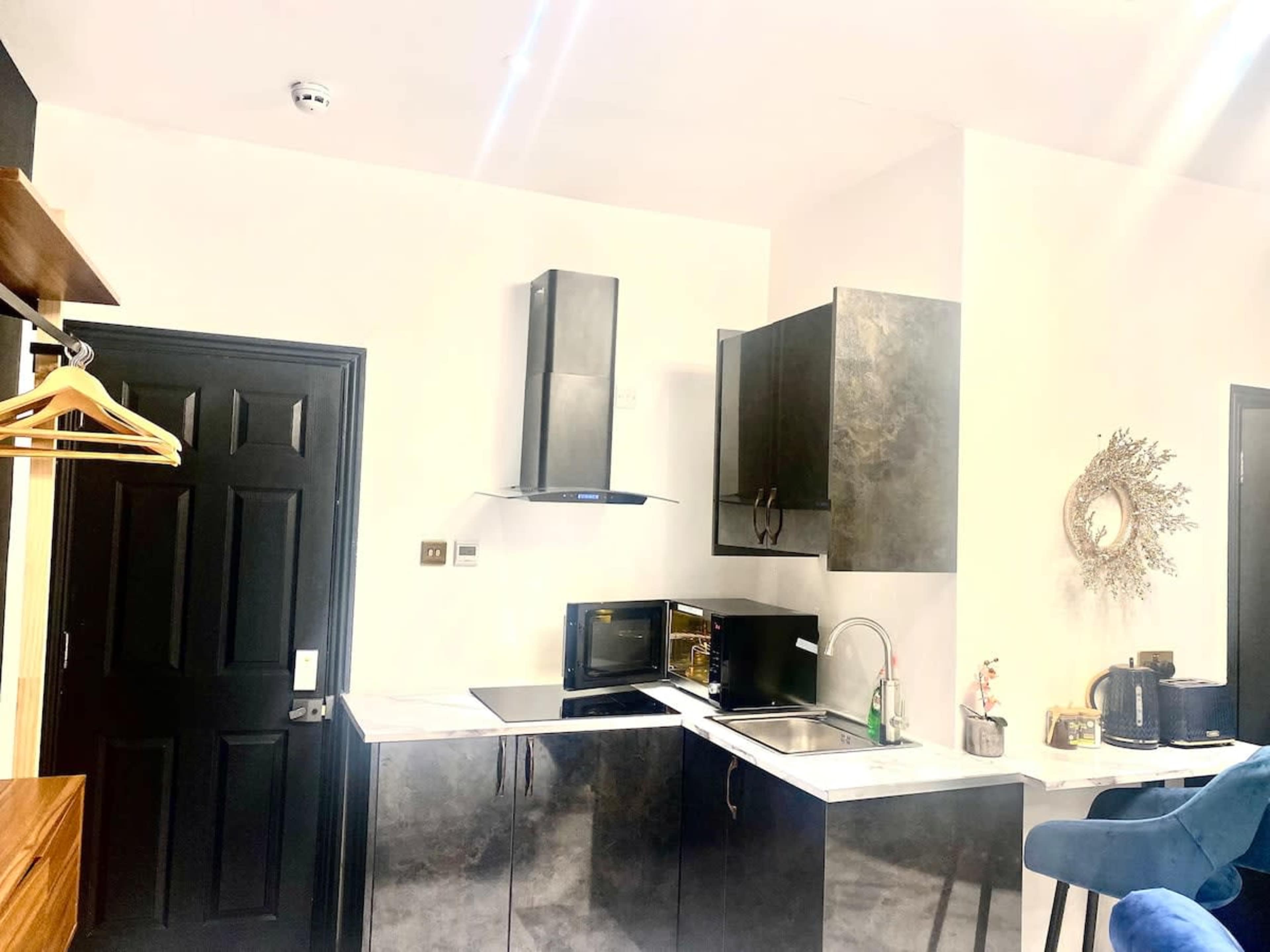 The image shows a modern kitchen with black cabinets, a stainless steel hood, a microwave, and a sink on a marble countertop.