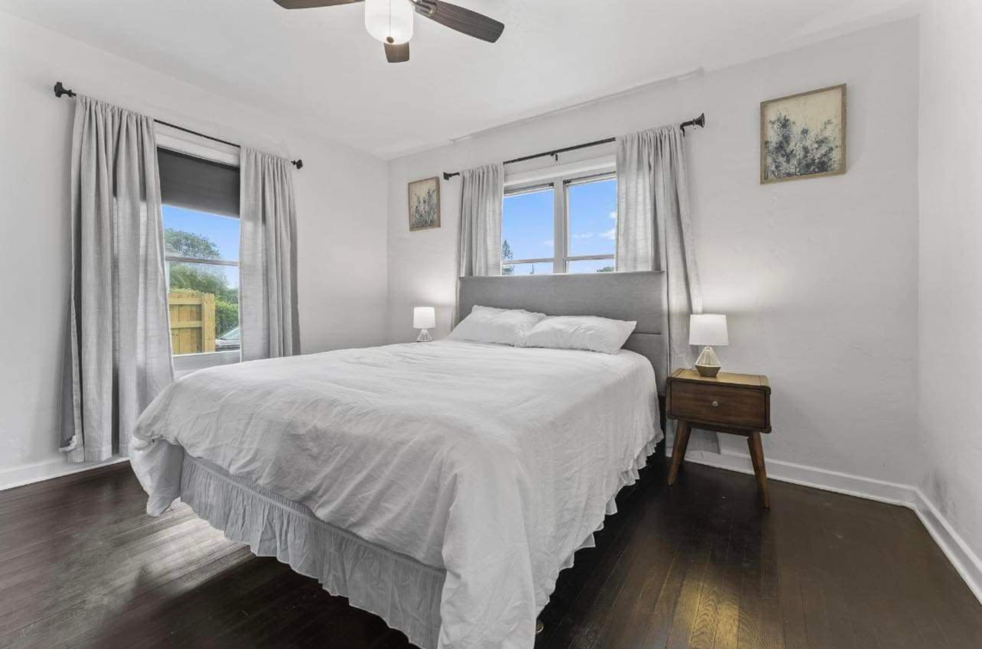 A neatly arranged bedroom with a bed, two lamps on nightstands, and window curtains.