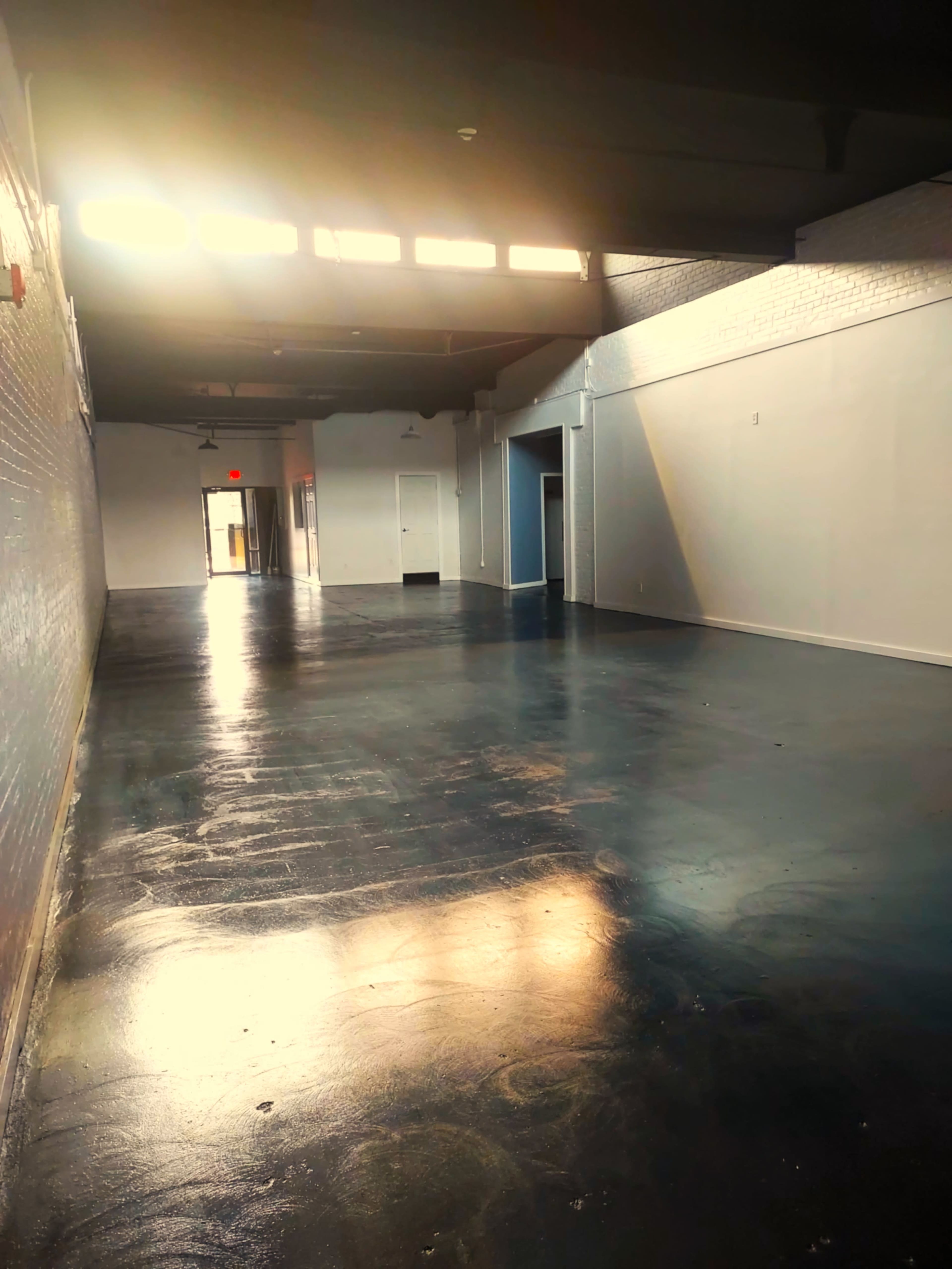 The image shows a long, empty hallway with polished floors and natural light streaming in from windows at the far end.