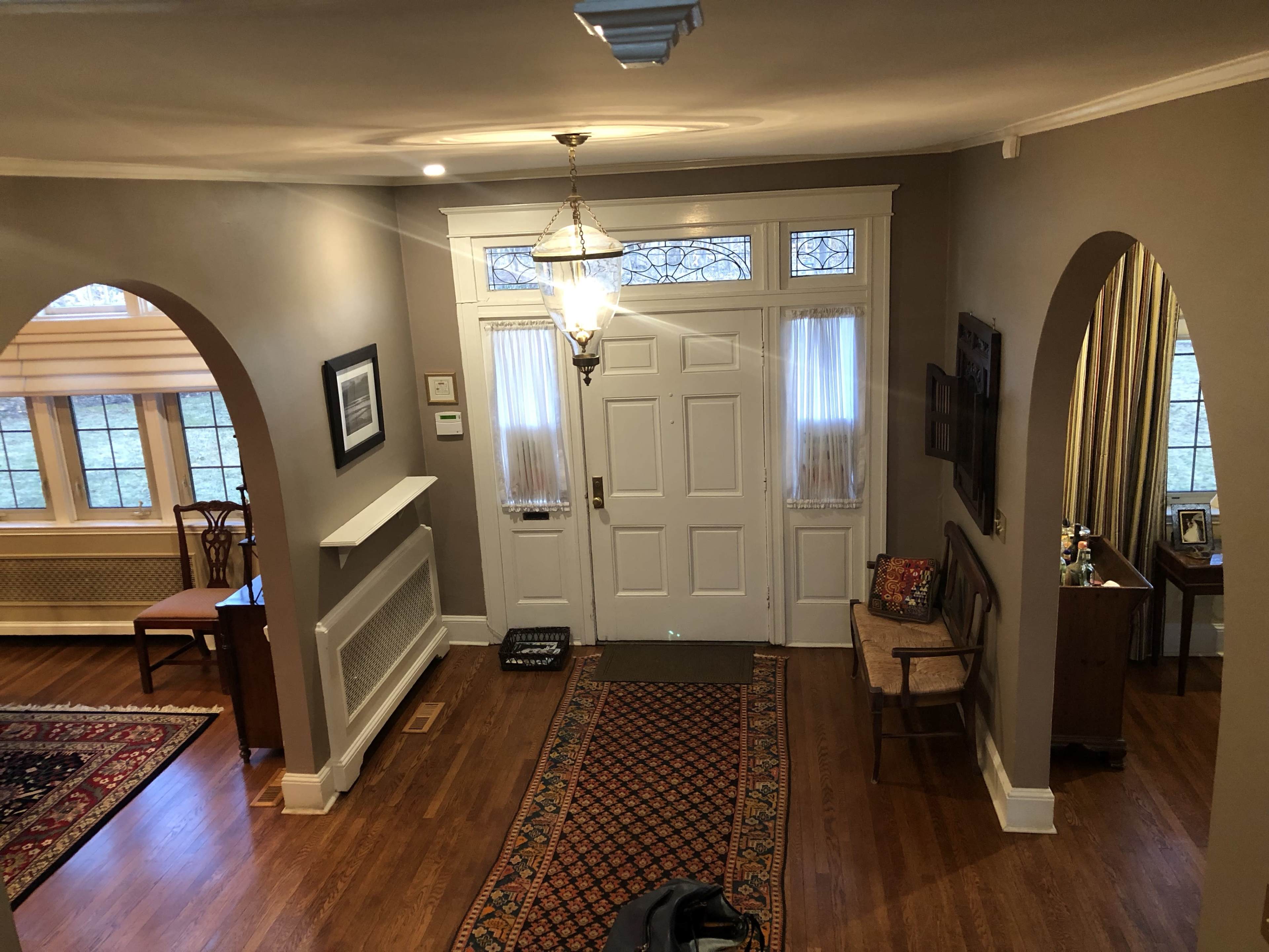 The image shows a spacious entryway with a chandelier, coat hooks, and arched doorways leading to different areas of the home.
