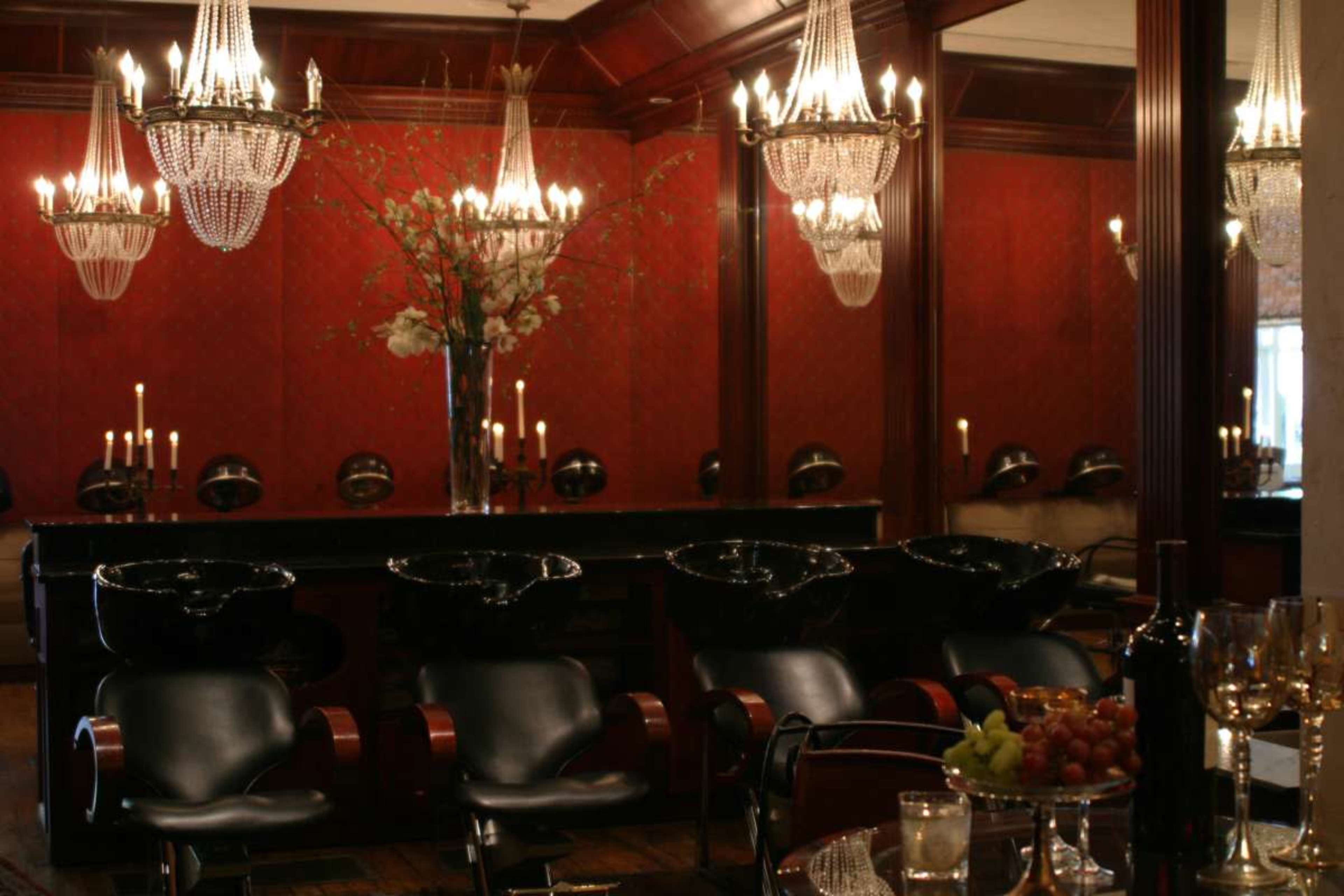 The image shows a luxurious salon interior with plush black shampoo chairs, elegant chandeliers, and rich red walls adorned with floral arrangements.