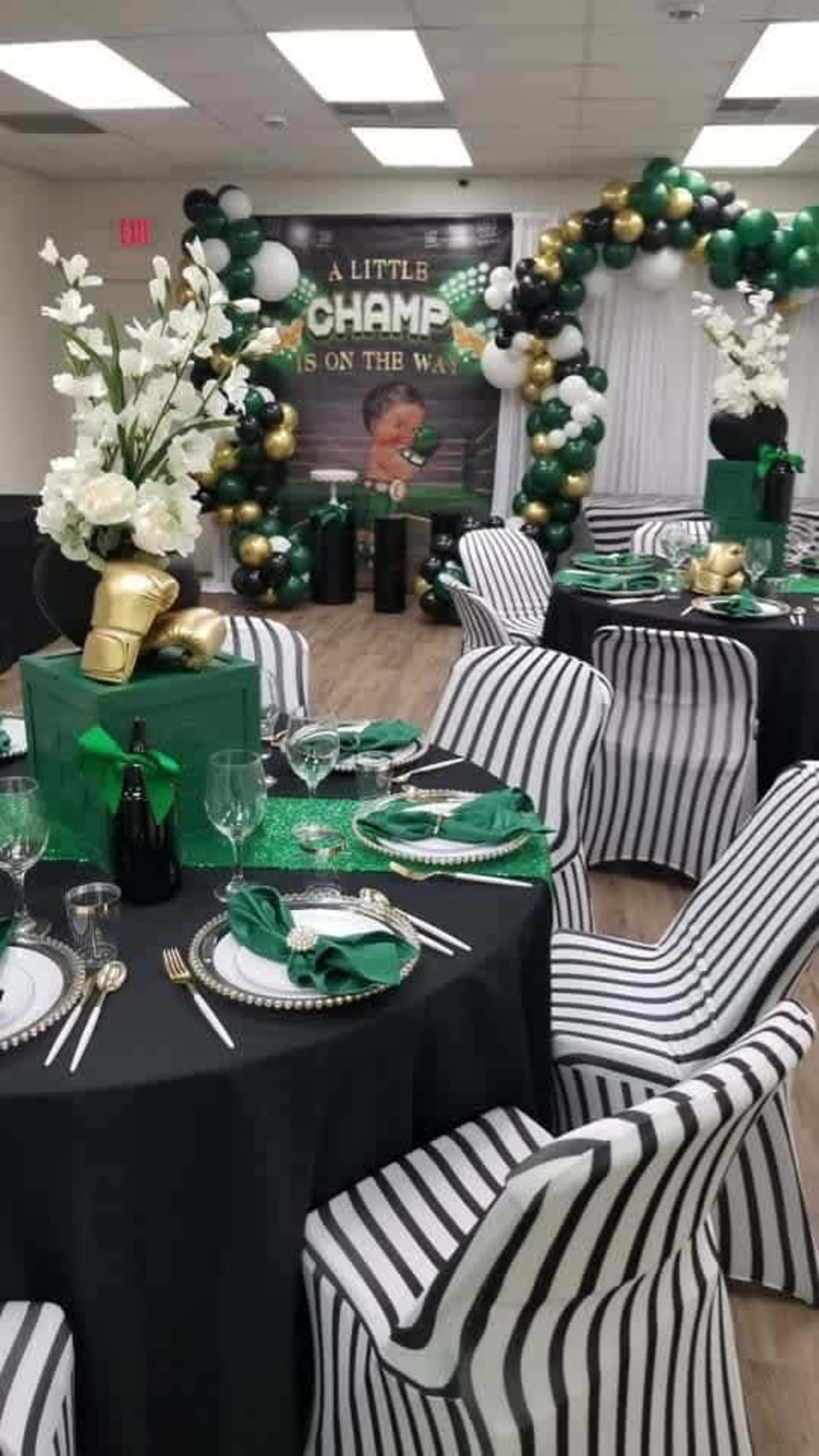 A decorated banquet room with black and white striped chairs, green and gold balloons, and elegant table settings for a celebration.
