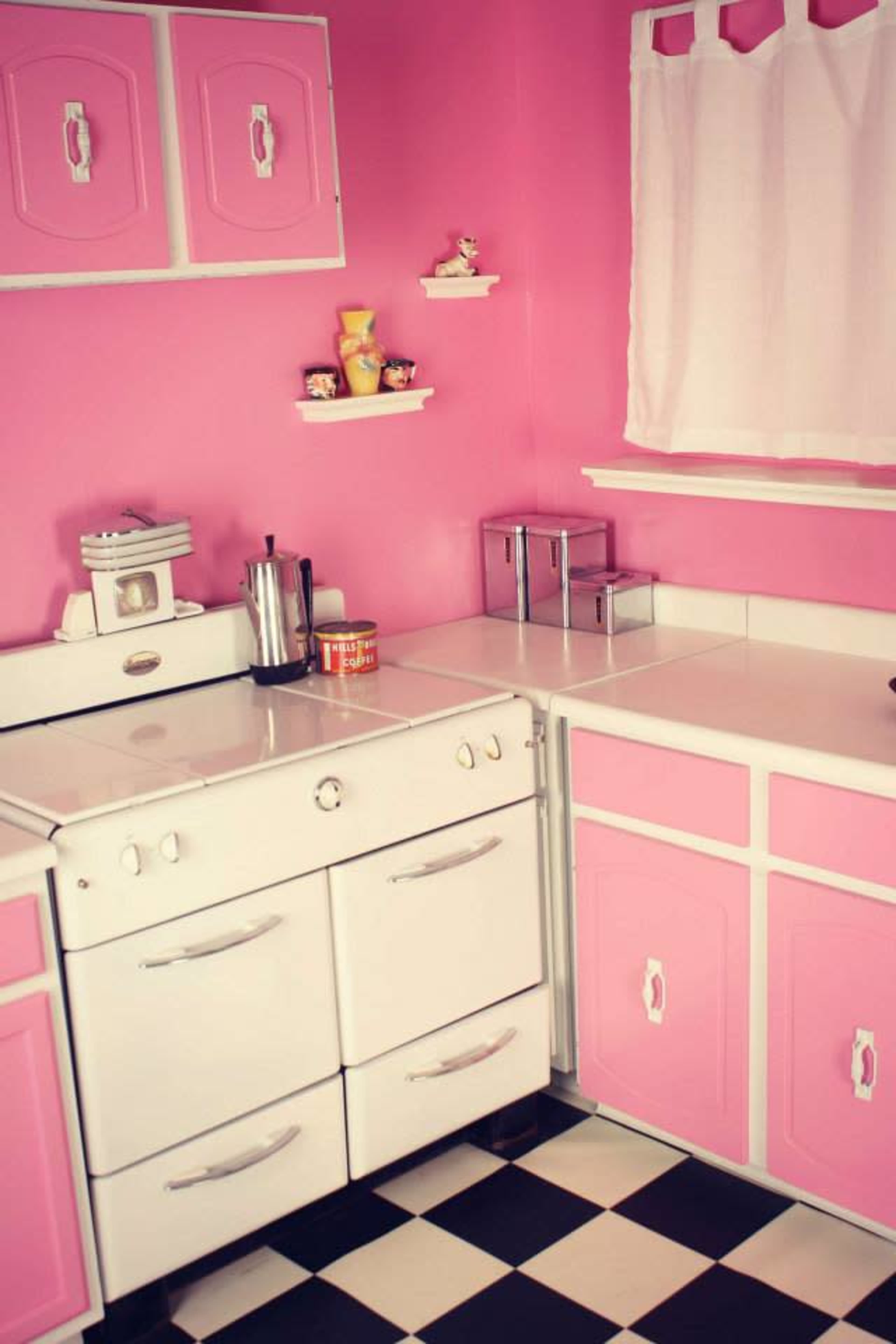 A vintage-style kitchen with pink walls, a white stove, and a black-and-white checked floor.