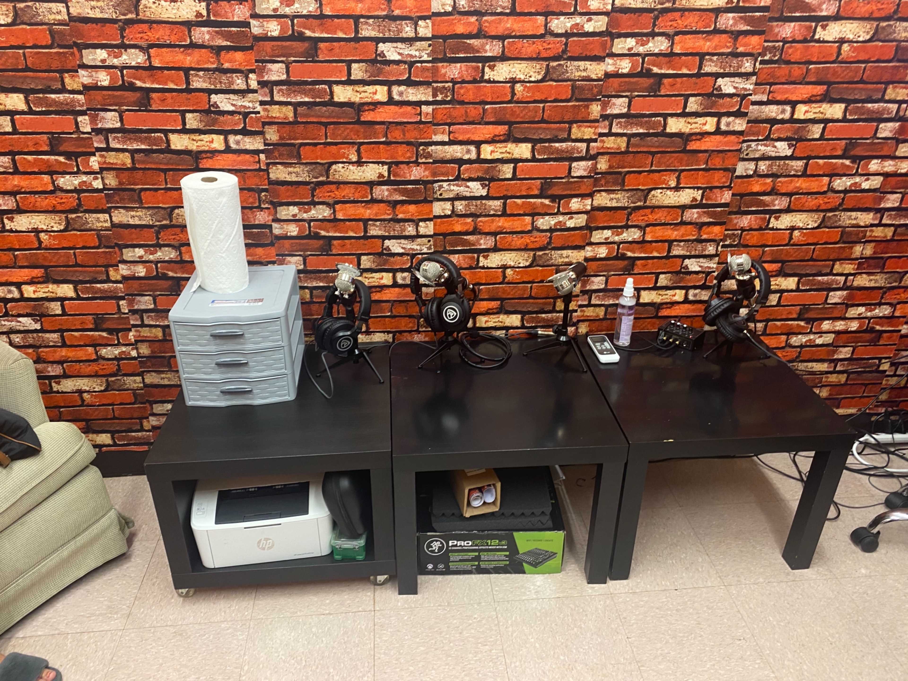 A wooden table with four headsets and a stack of storage drawers is positioned against a brick-patterned wall.