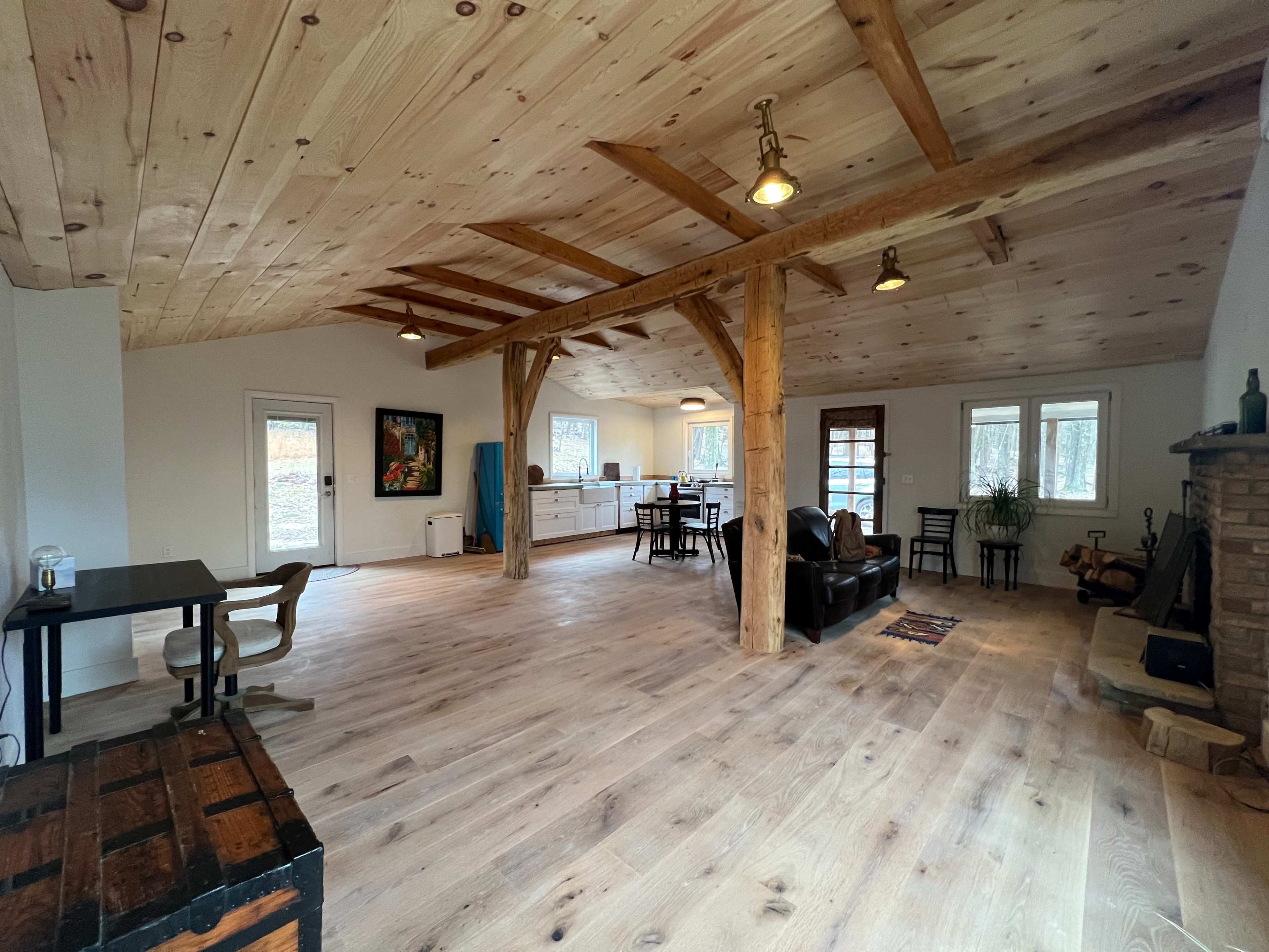 An open-concept room with wooden beams, a stone fireplace, and a combination of dining and living areas.