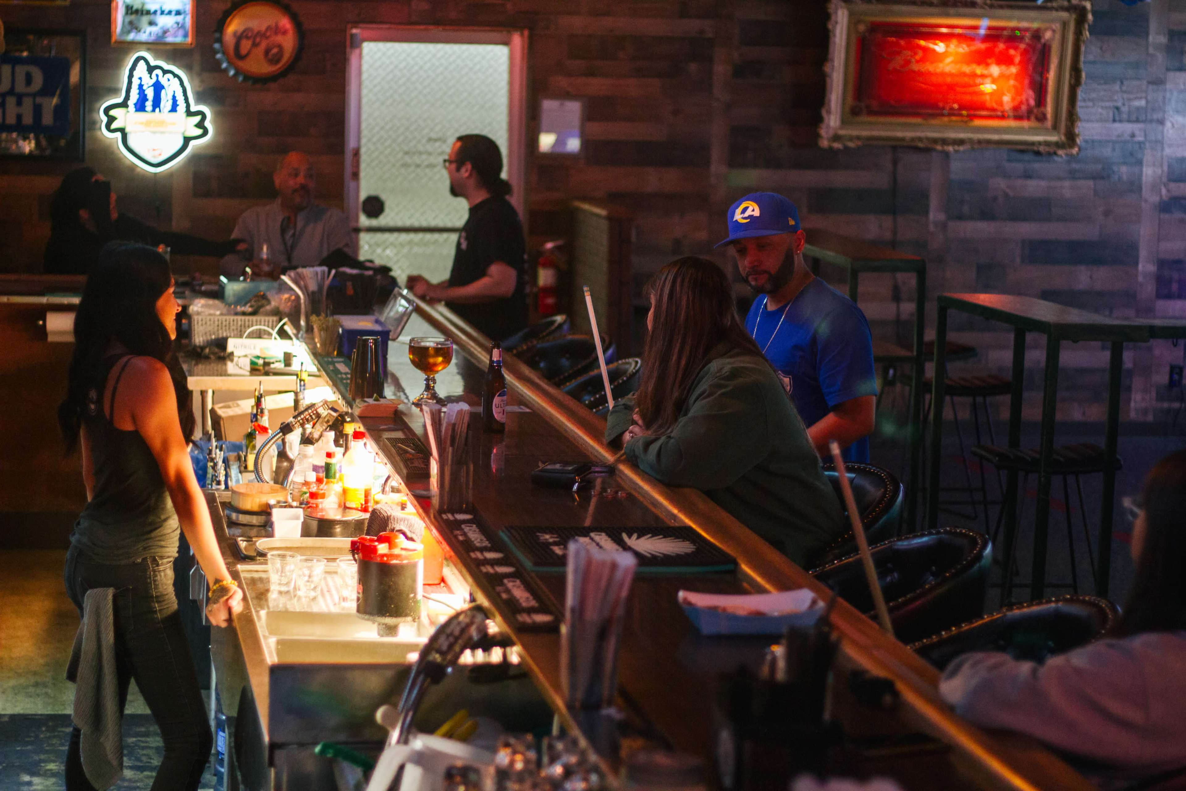 A bar scene features a bartender serving drinks while patrons engage in conversation at the bar.