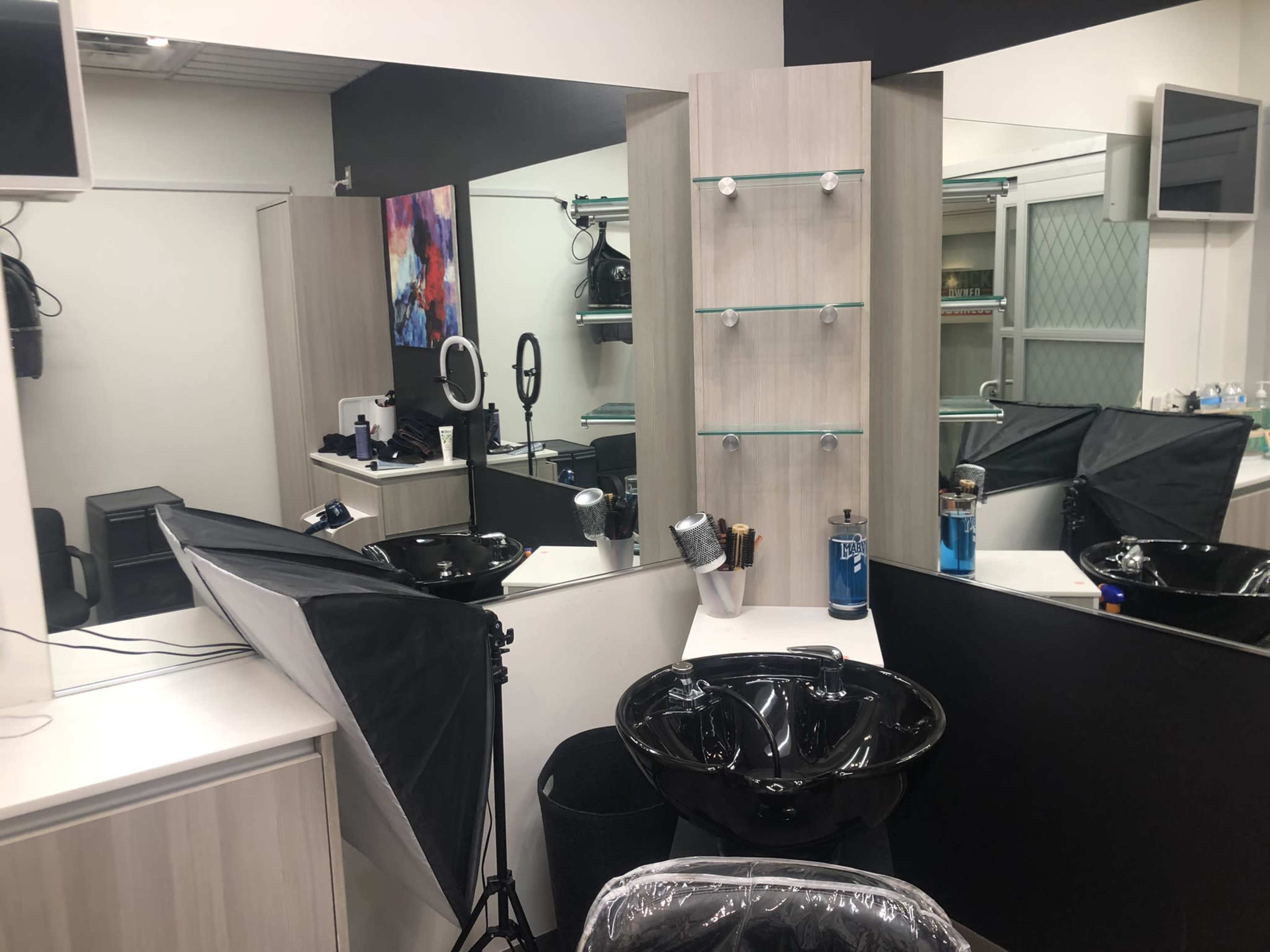 A hair salon interior with a black wash station, multiple mirrors, and styling tools arranged neatly on a counter.