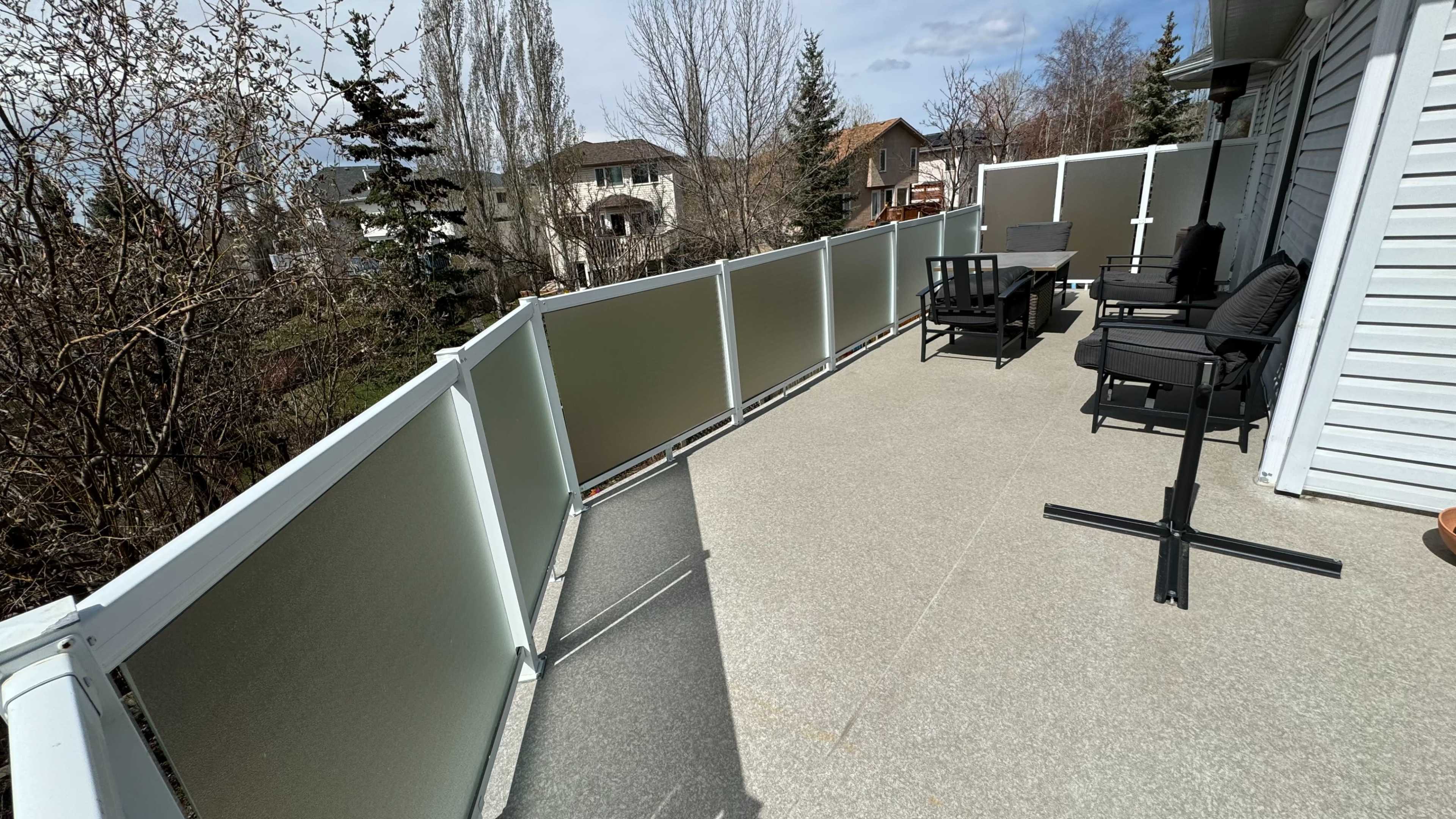 A spacious balcony with outdoor furniture and a railing overlooking nearby houses and trees.