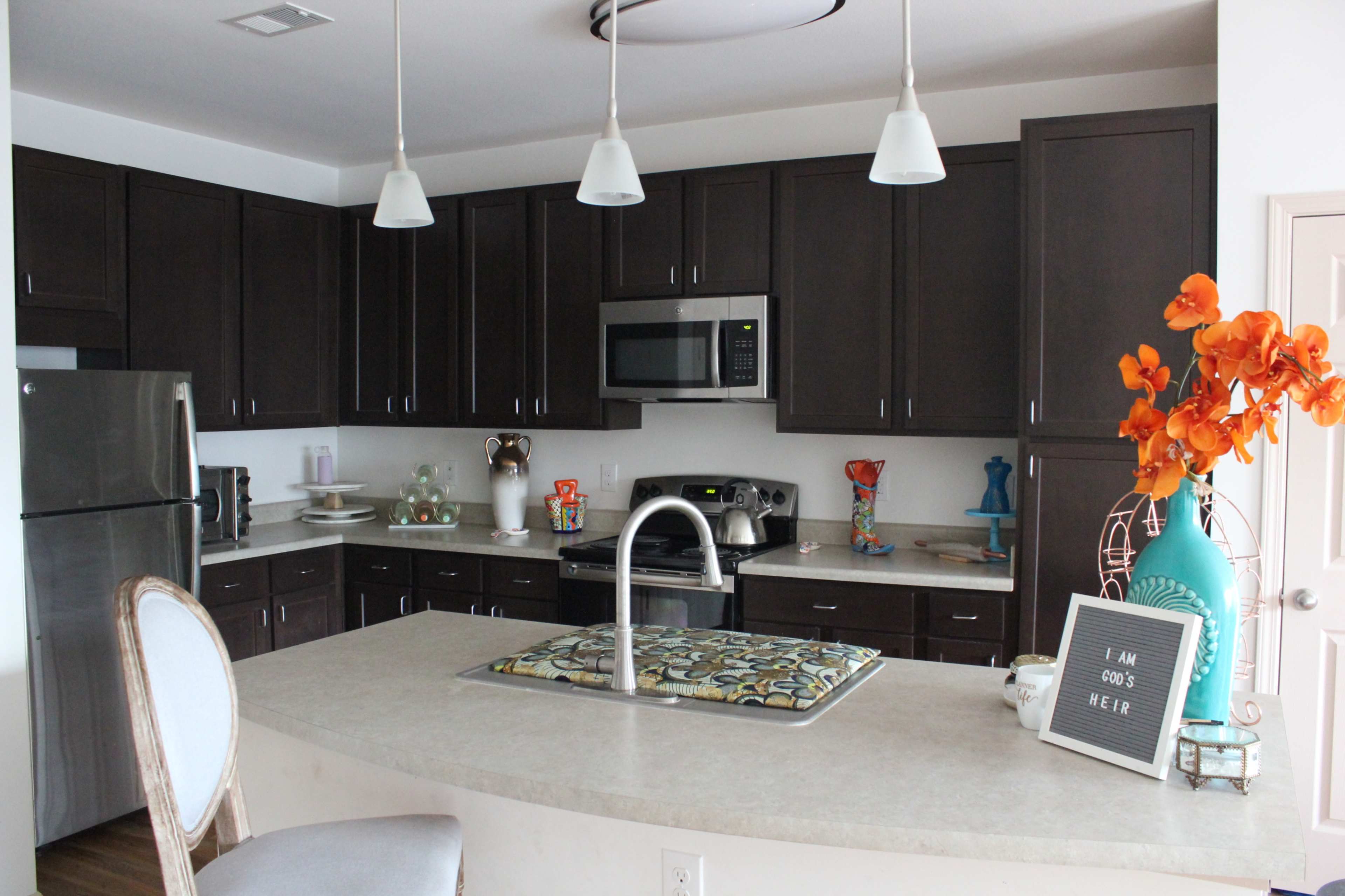 A modern kitchen with dark cabinets, stainless steel appliances, and a central island featuring decorative items and a vase of orange flowers.