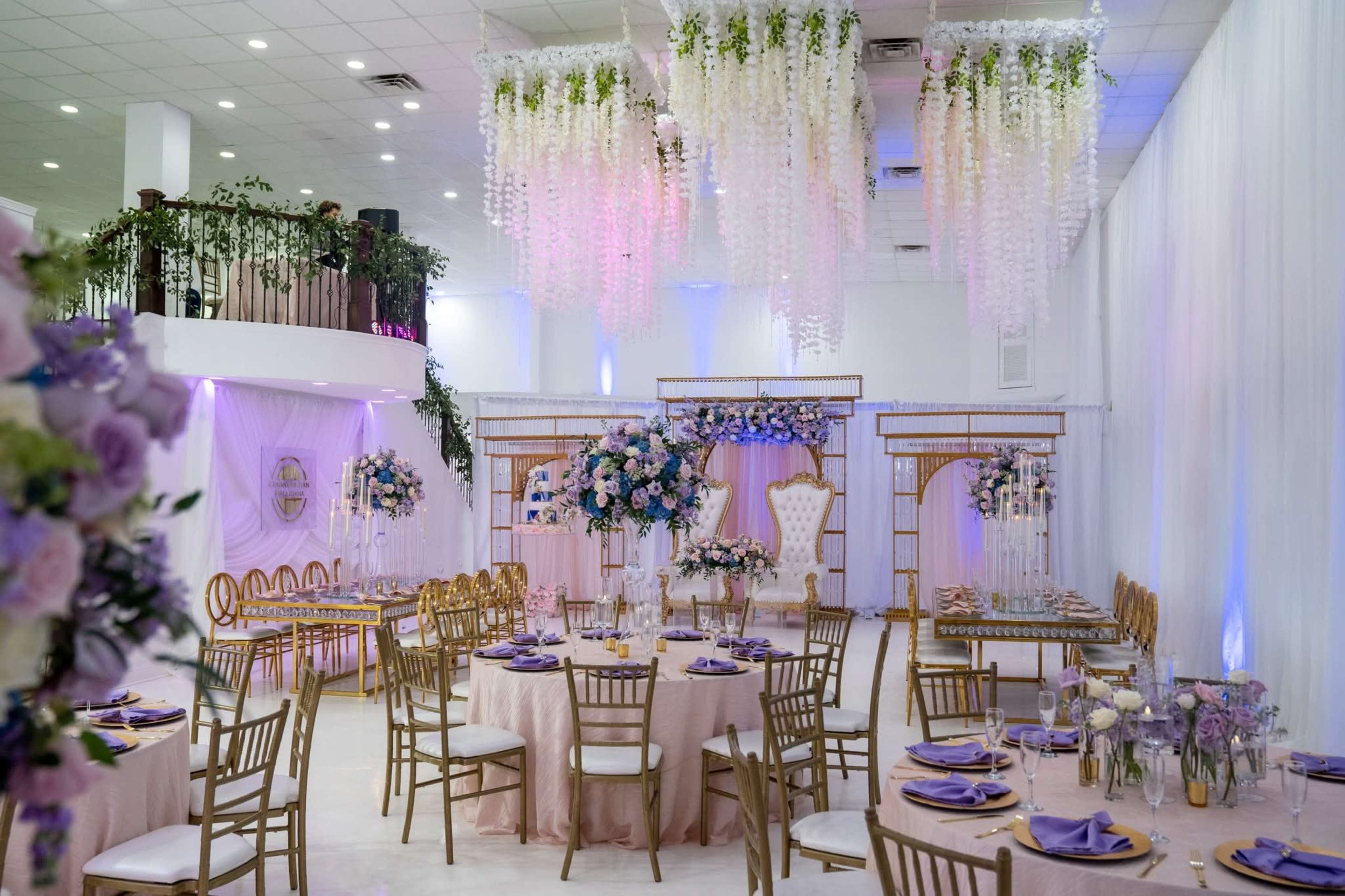 The image shows an elegantly decorated banquet hall with floral arrangements, round tables set with purple tableware, and draped ceiling decorations.