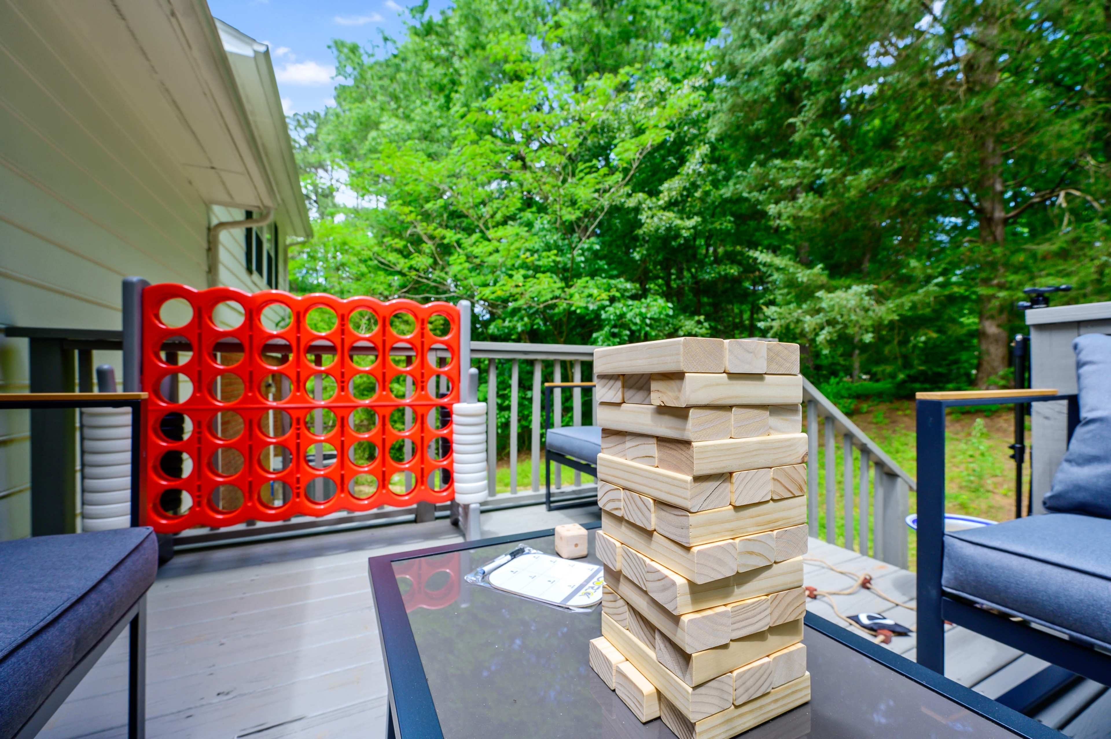 A wooden deck features a Jenga tower, a Connect Four game, and two seating areas surrounded by trees.