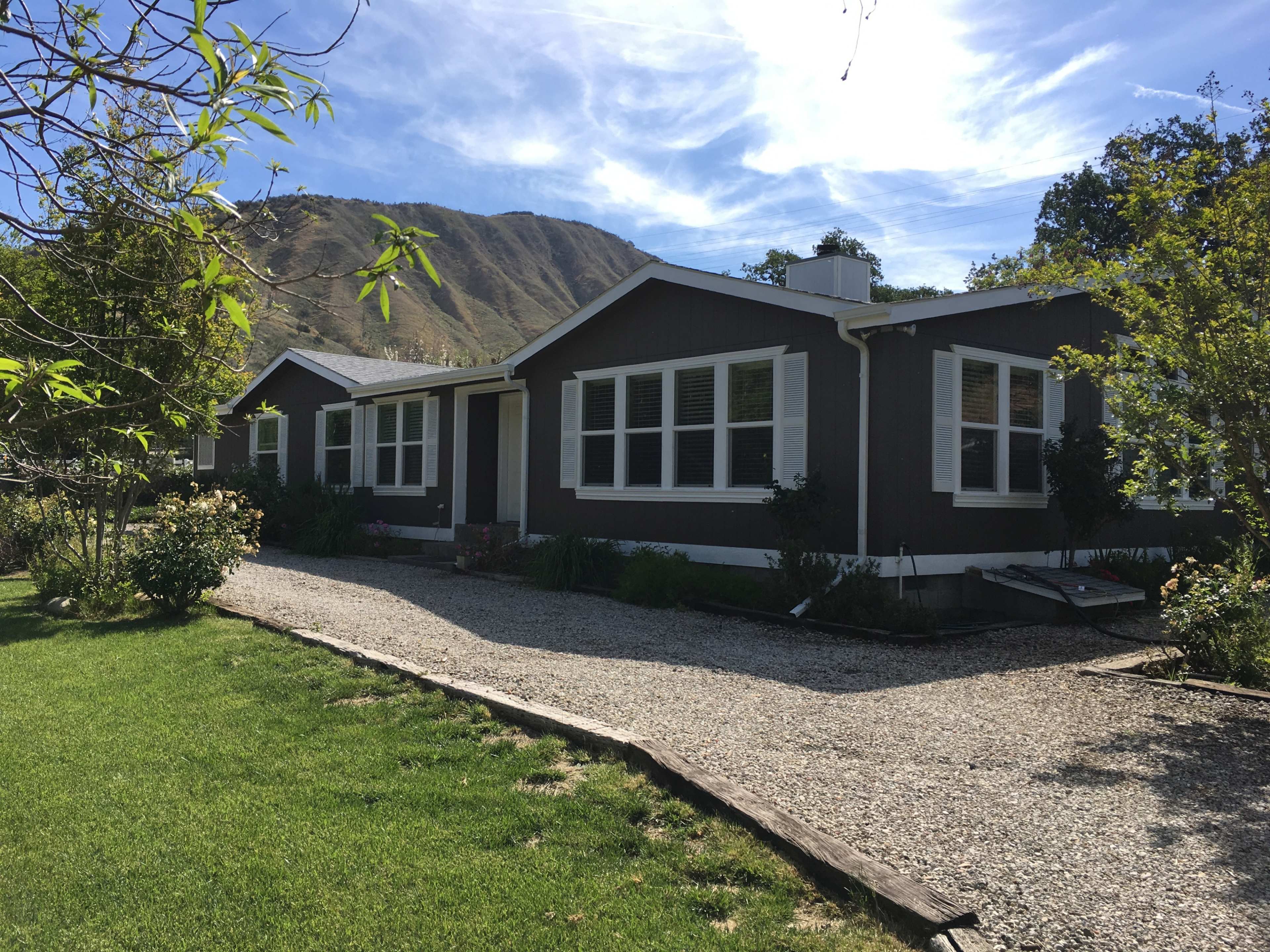 A single-story house with a gravel driveway is set against a mountainous backdrop.
