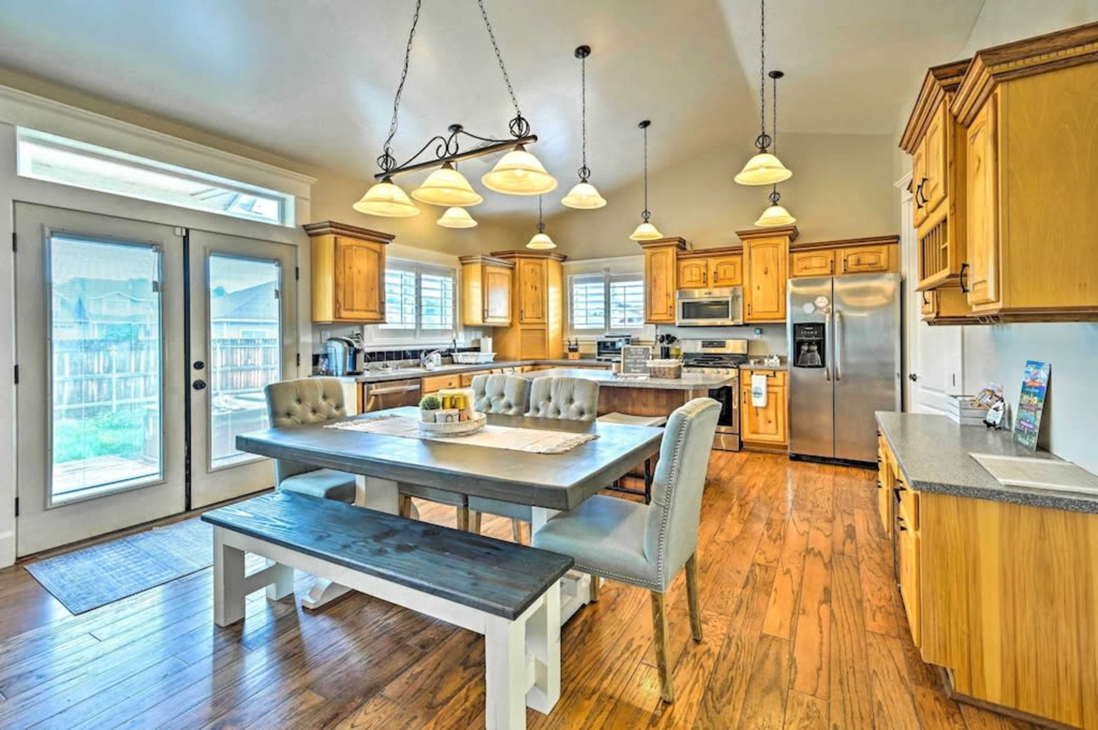 A spacious kitchen features wooden cabinetry, a large dining table with seating, and modern appliances, with natural light coming through patio doors.