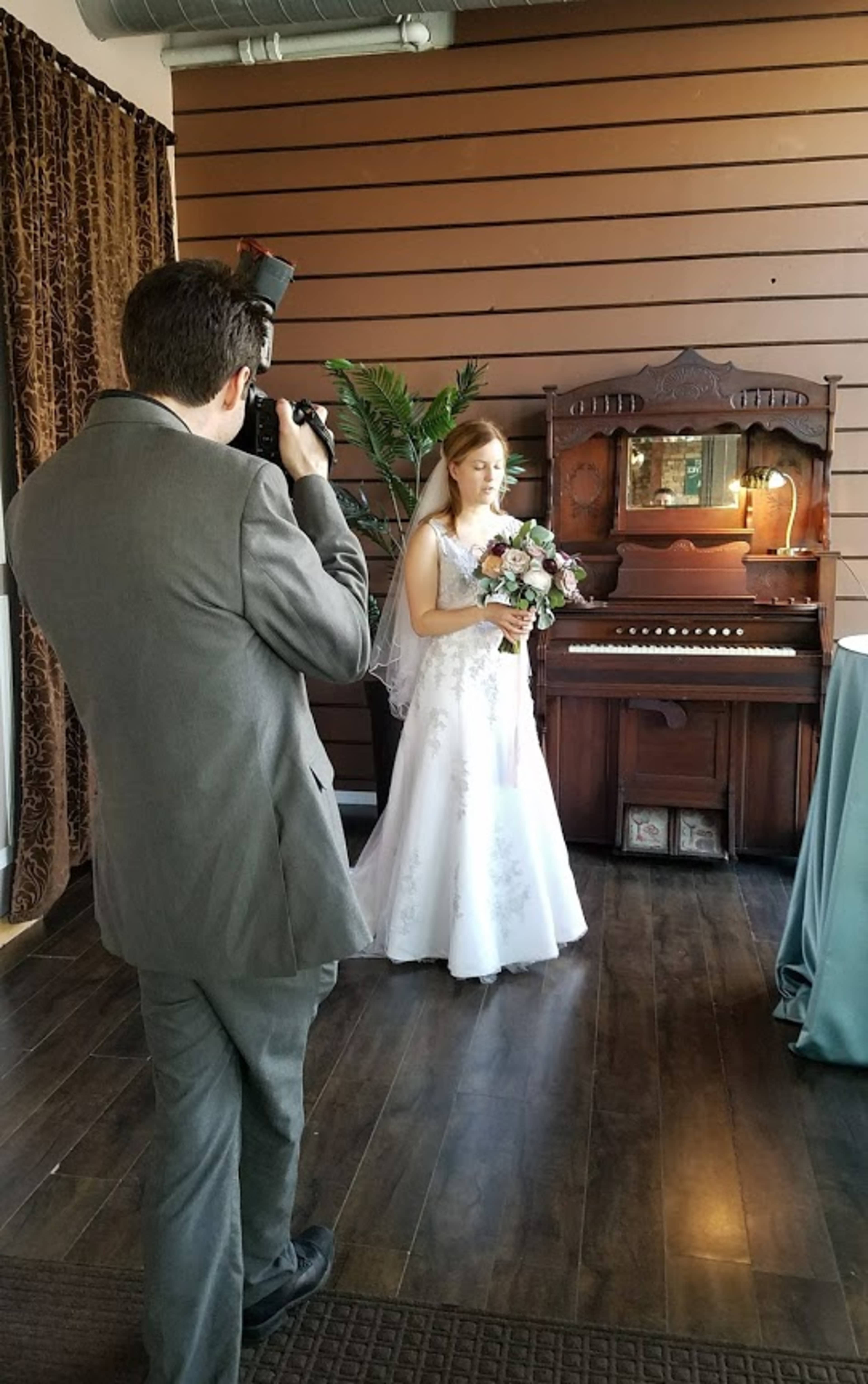 A bride in a white gown poses with a bouquet while a photographer captures the moment in a decorated indoor setting.