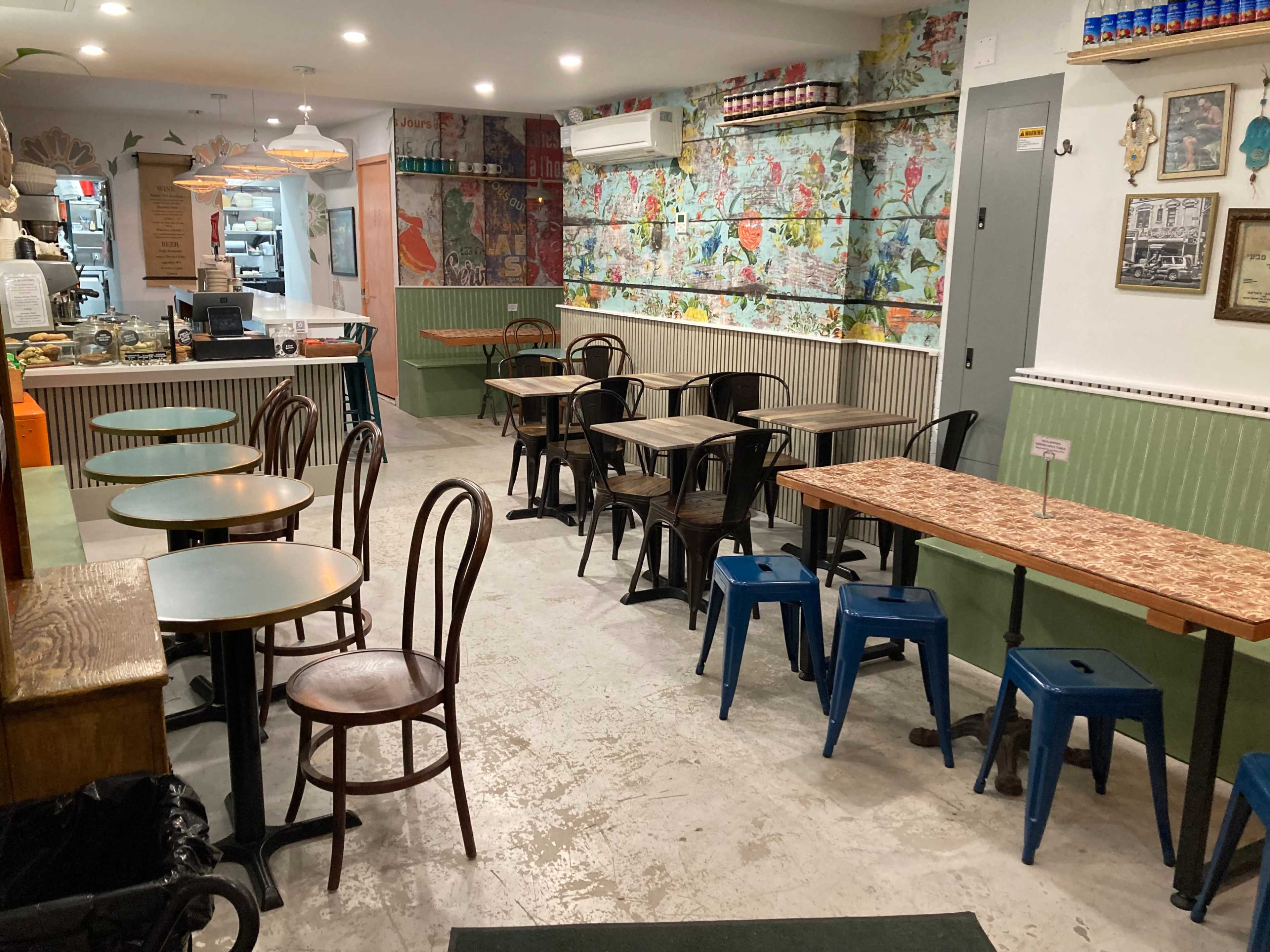 The image shows a colorful café interior with wooden and metal tables and chairs, a service counter at the back, and decorative wall murals.