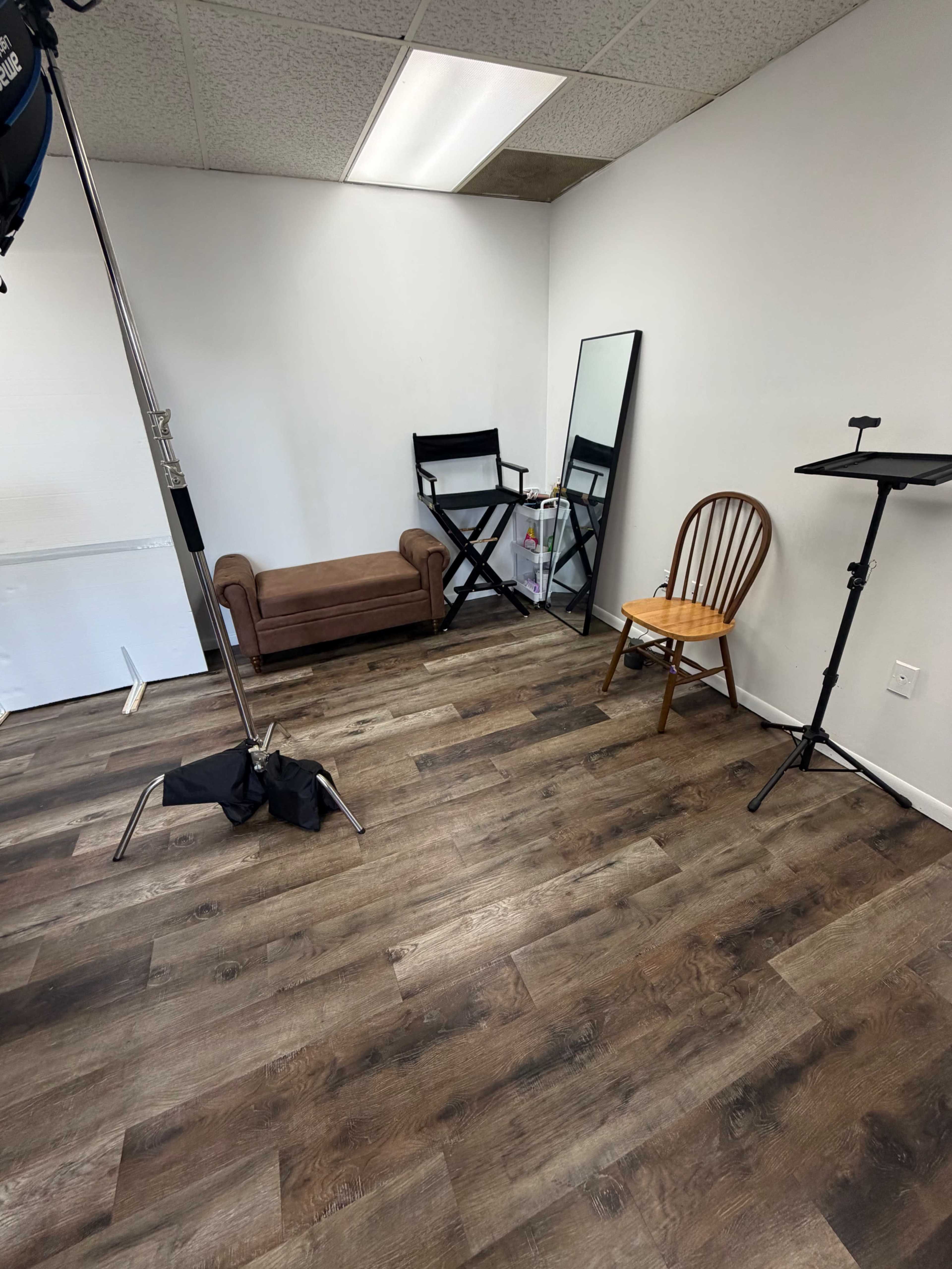 The image shows an empty room with wooden flooring, a brown couch, a floor mirror, a wooden chair, and a music stand.