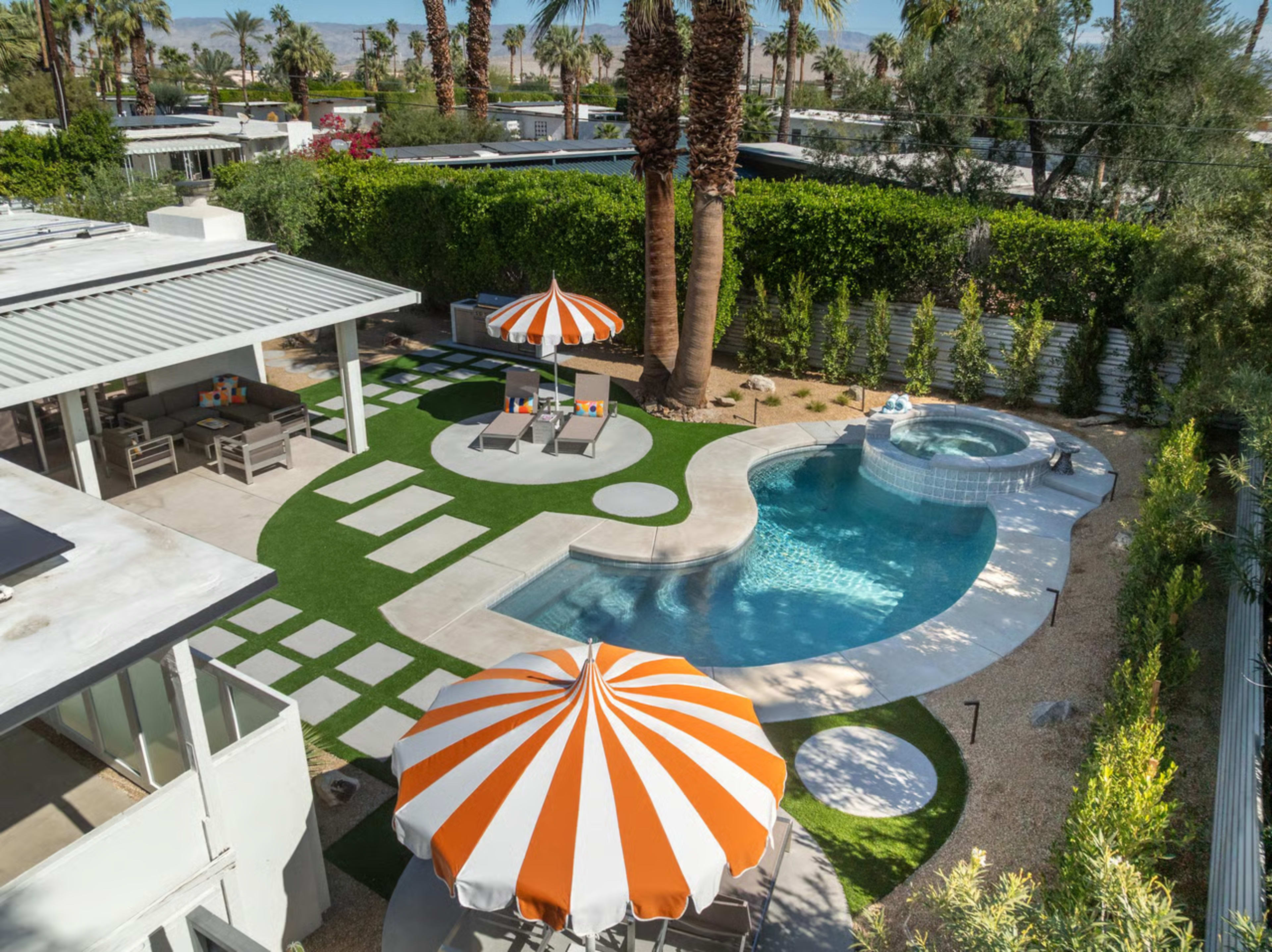 The image depicts a backyard with a swimming pool, lounge chairs, an umbrella, and a hot tub, surrounded by palm trees and landscaped grass.