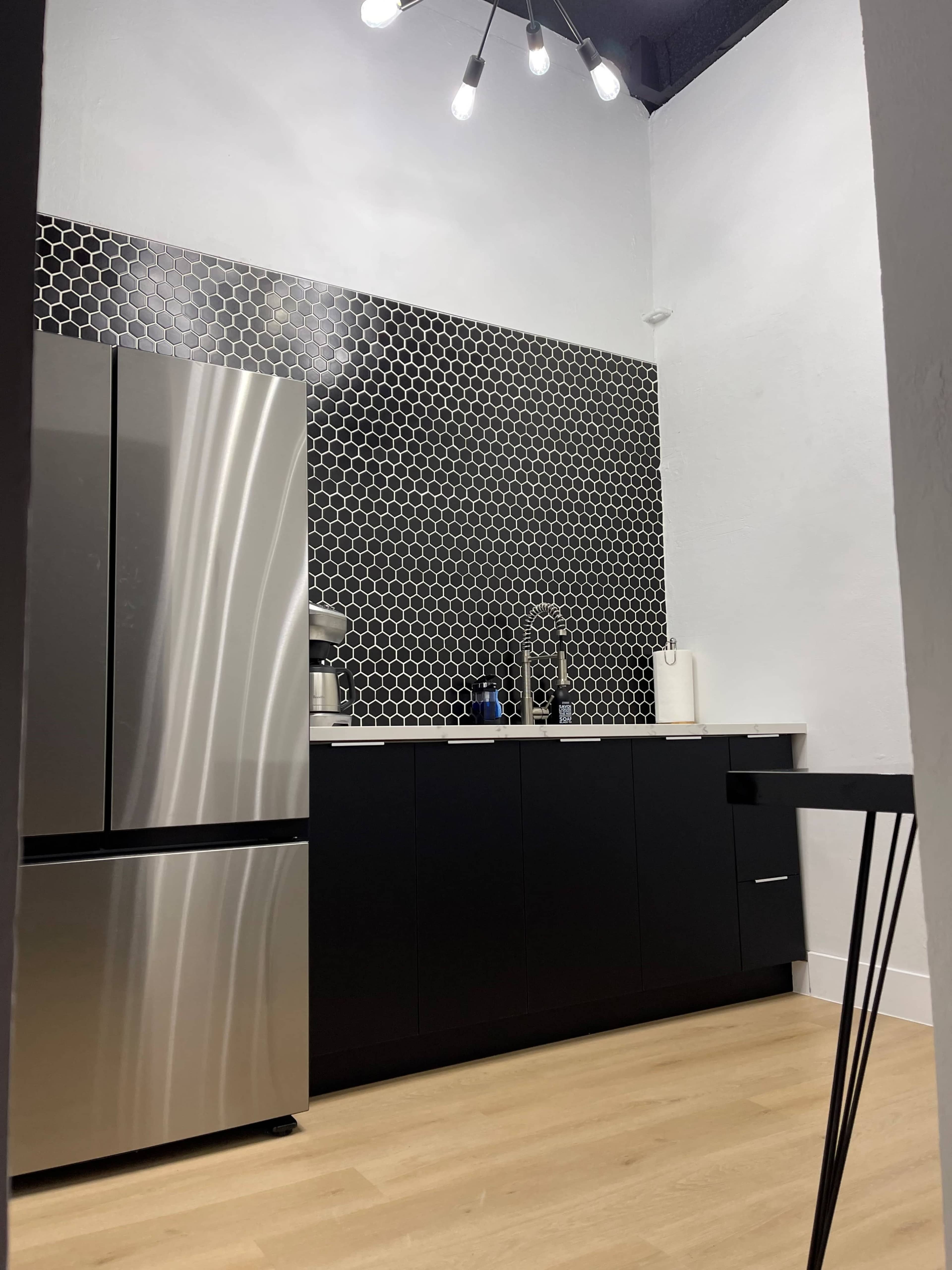 A modern kitchen features a stainless steel refrigerator, black cabinetry, and a hexagonal tile backsplash.