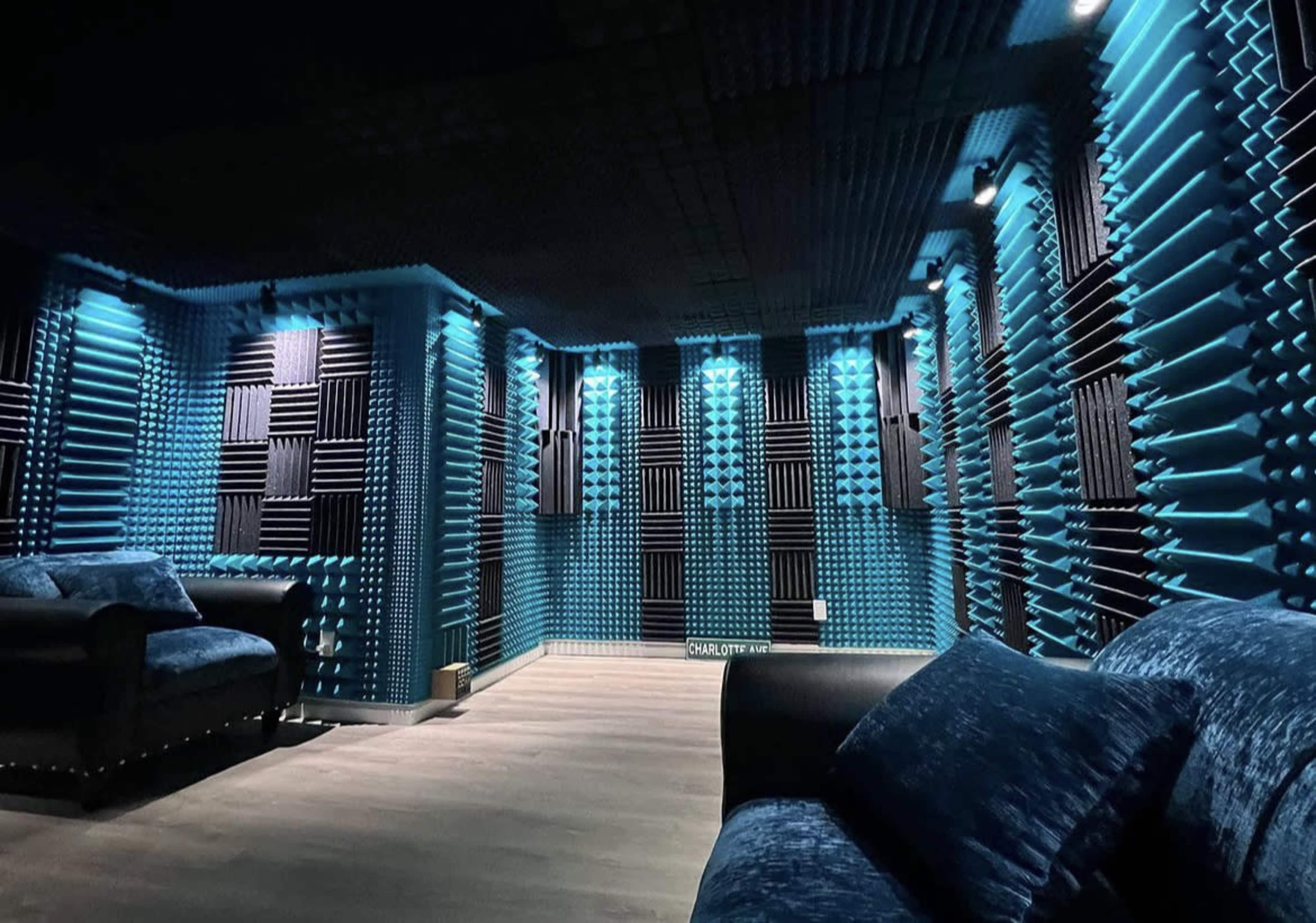 A soundproof studio room with acoustic foam panels on the walls and a blue color scheme, featuring a seating area with dark blue couches.