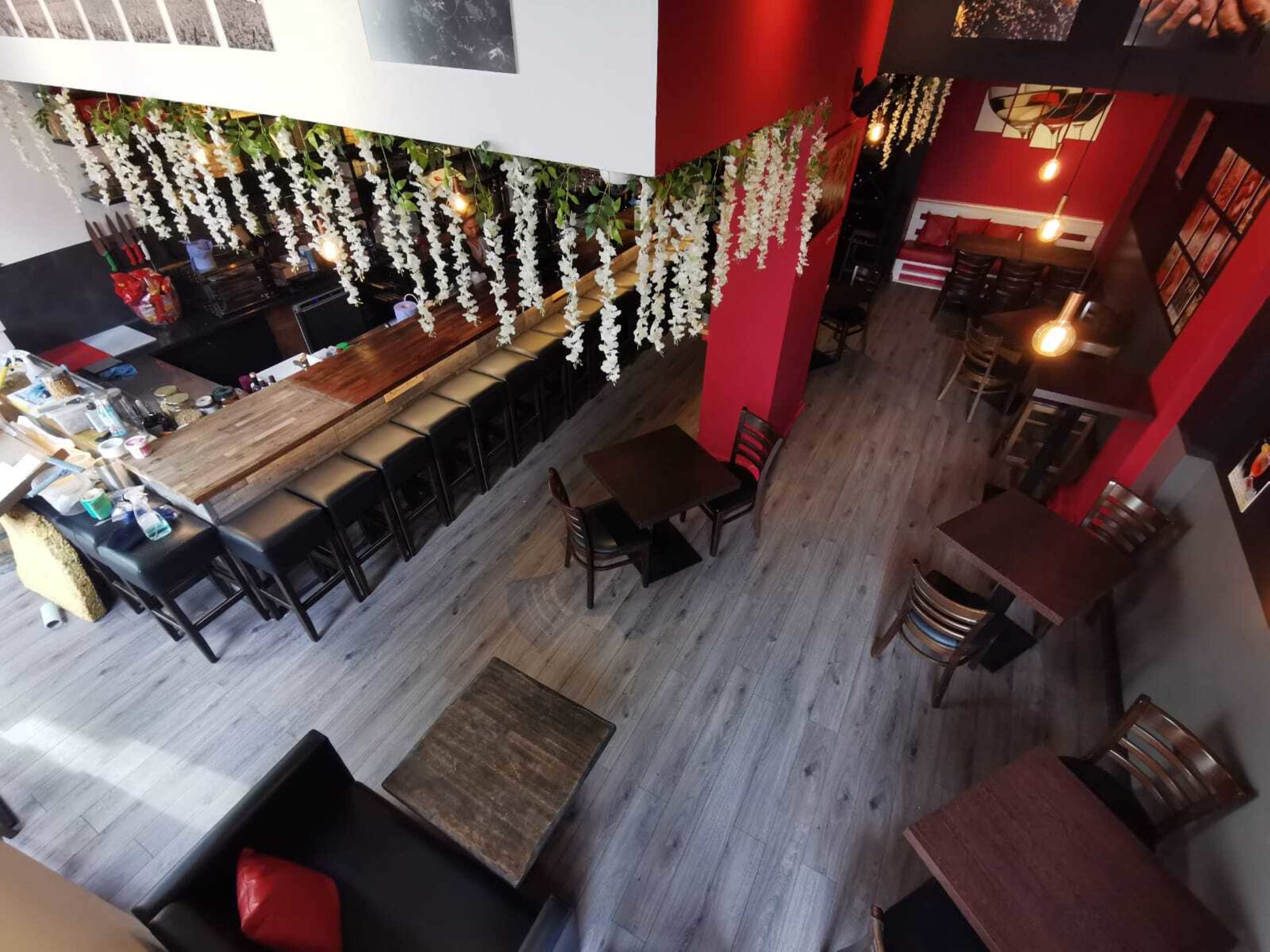 A cozy café interior with wooden tables, black chairs, and hanging floral decorations from the ceiling.