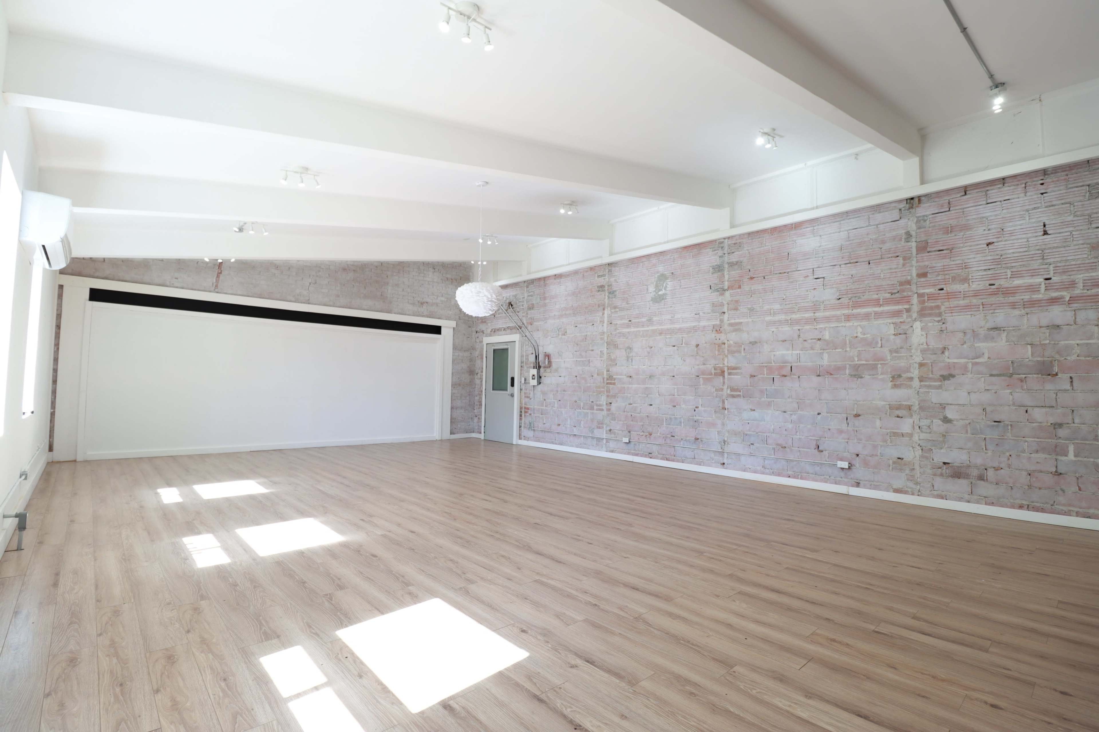 A spacious, brightly lit interior room with exposed brick walls and wooden flooring.