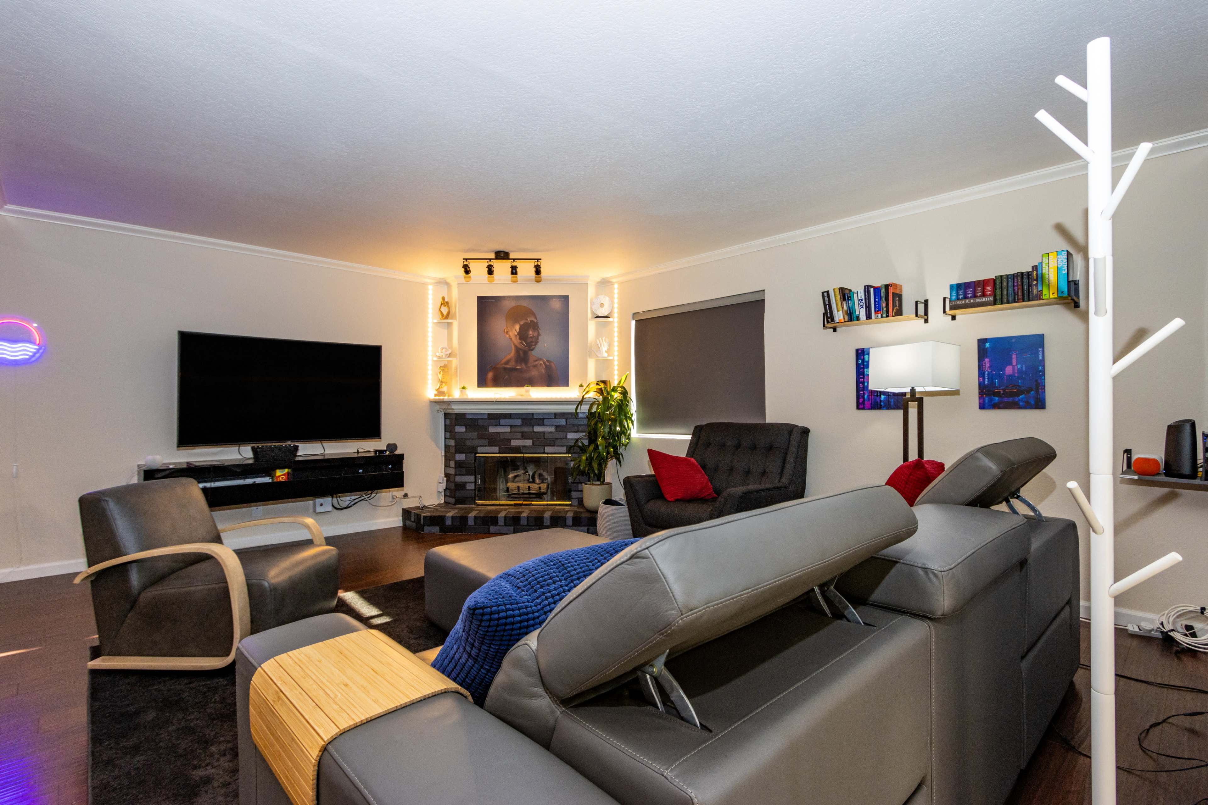 A modern living room featuring a fireplace, a large television mounted on the wall, and comfortable seating arrangements with a decorative bookshelf in the background.