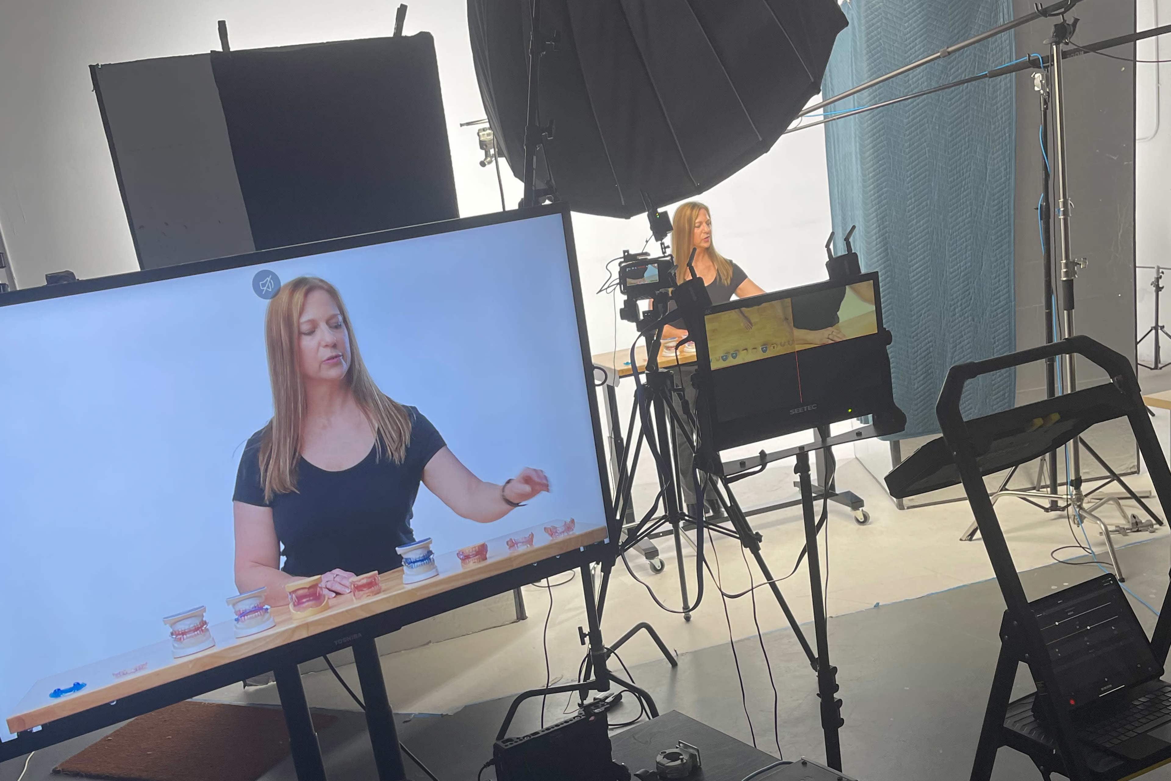 A woman is demonstrating products in a studio setting, with cameras and lighting equipment positioned around her.