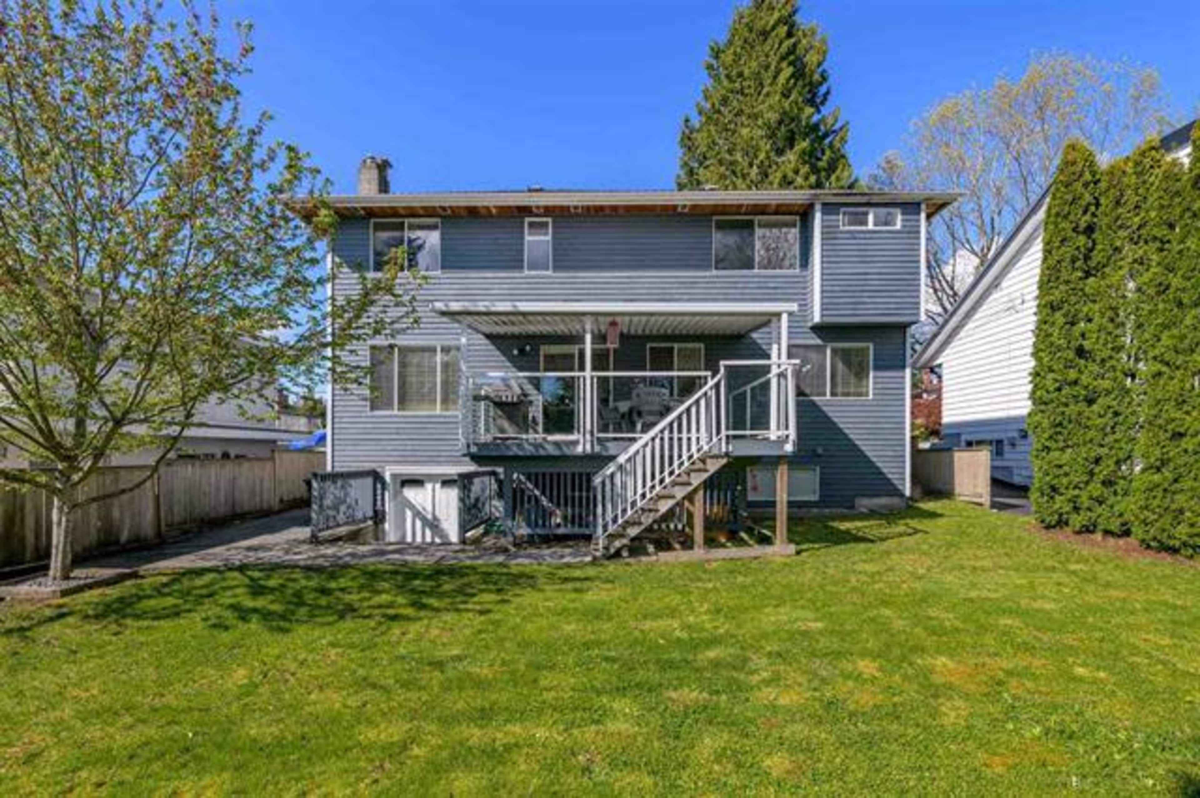 The back exterior of a two-story house with a deck and a well-maintained grassy yard, surrounded by trees and neighboring homes.
