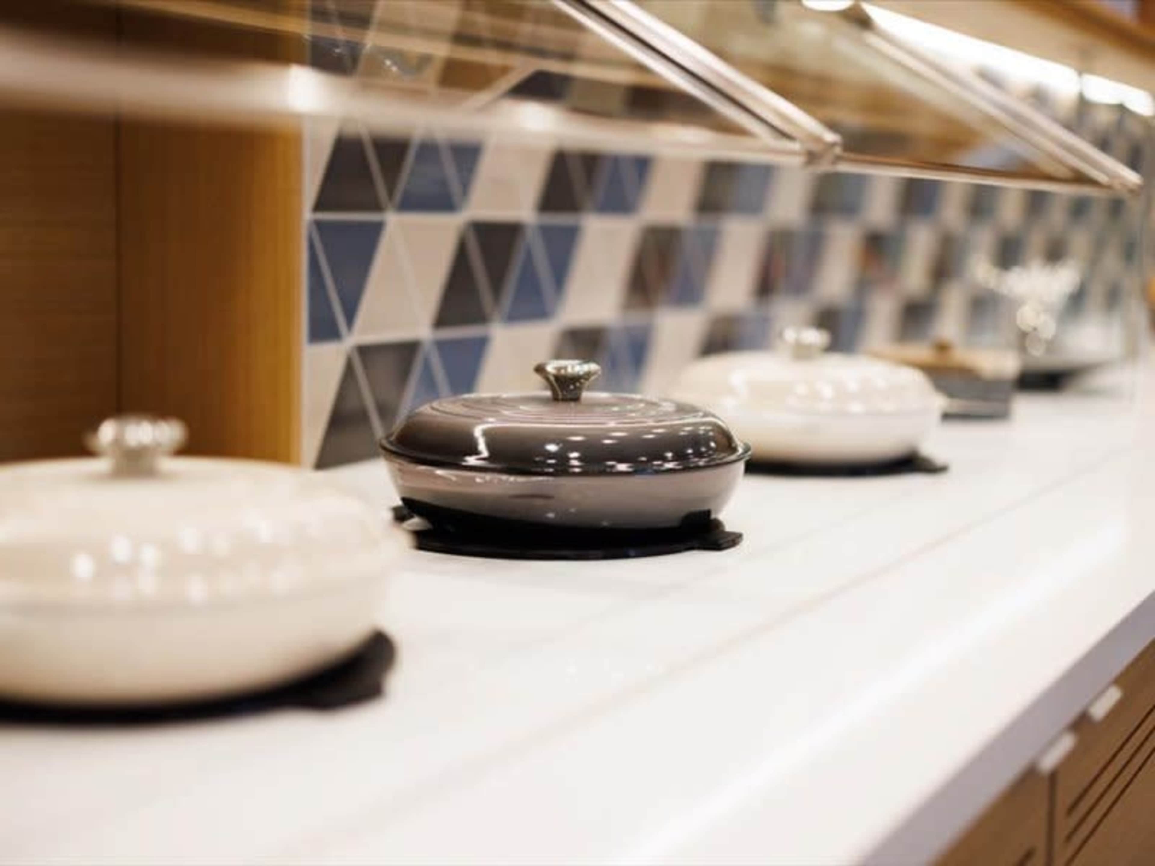 The image shows a row of covered serving dishes on a countertop, with a patterned tile backsplash in the background.