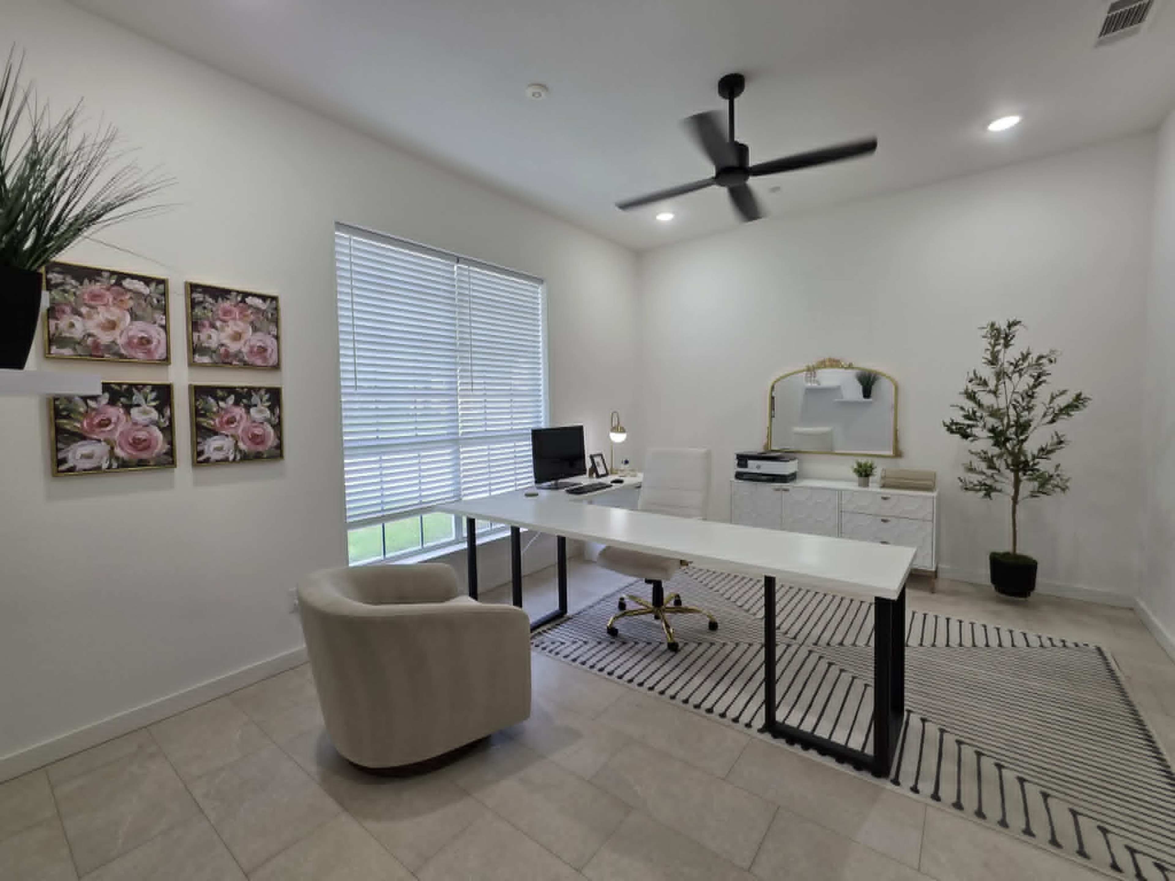 The image shows a modern office space with a white desk, a computer, a chair, a decorative plant, and artwork on the walls.