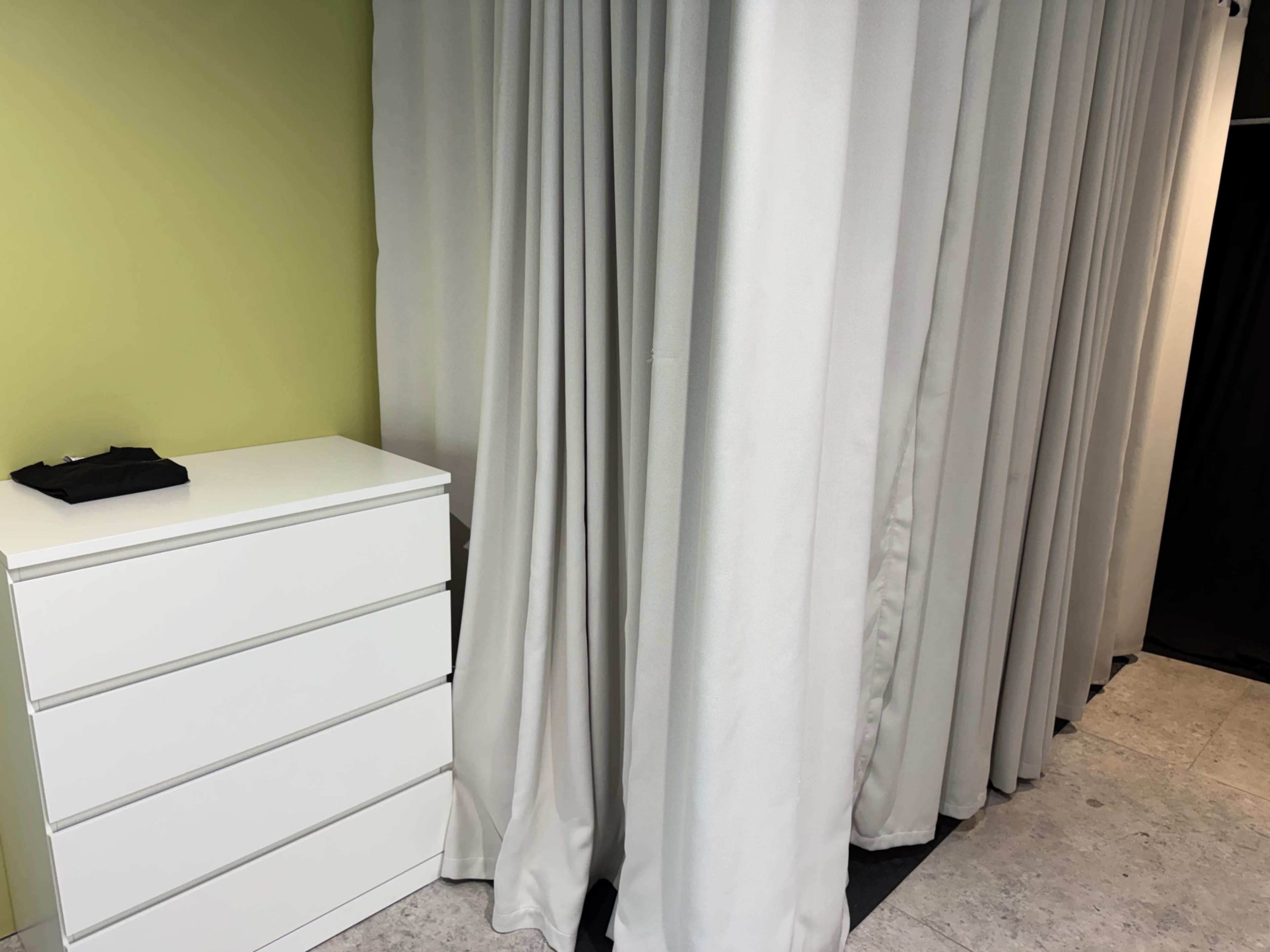 The image shows a white dresser next to a set of white curtains on a green wall.