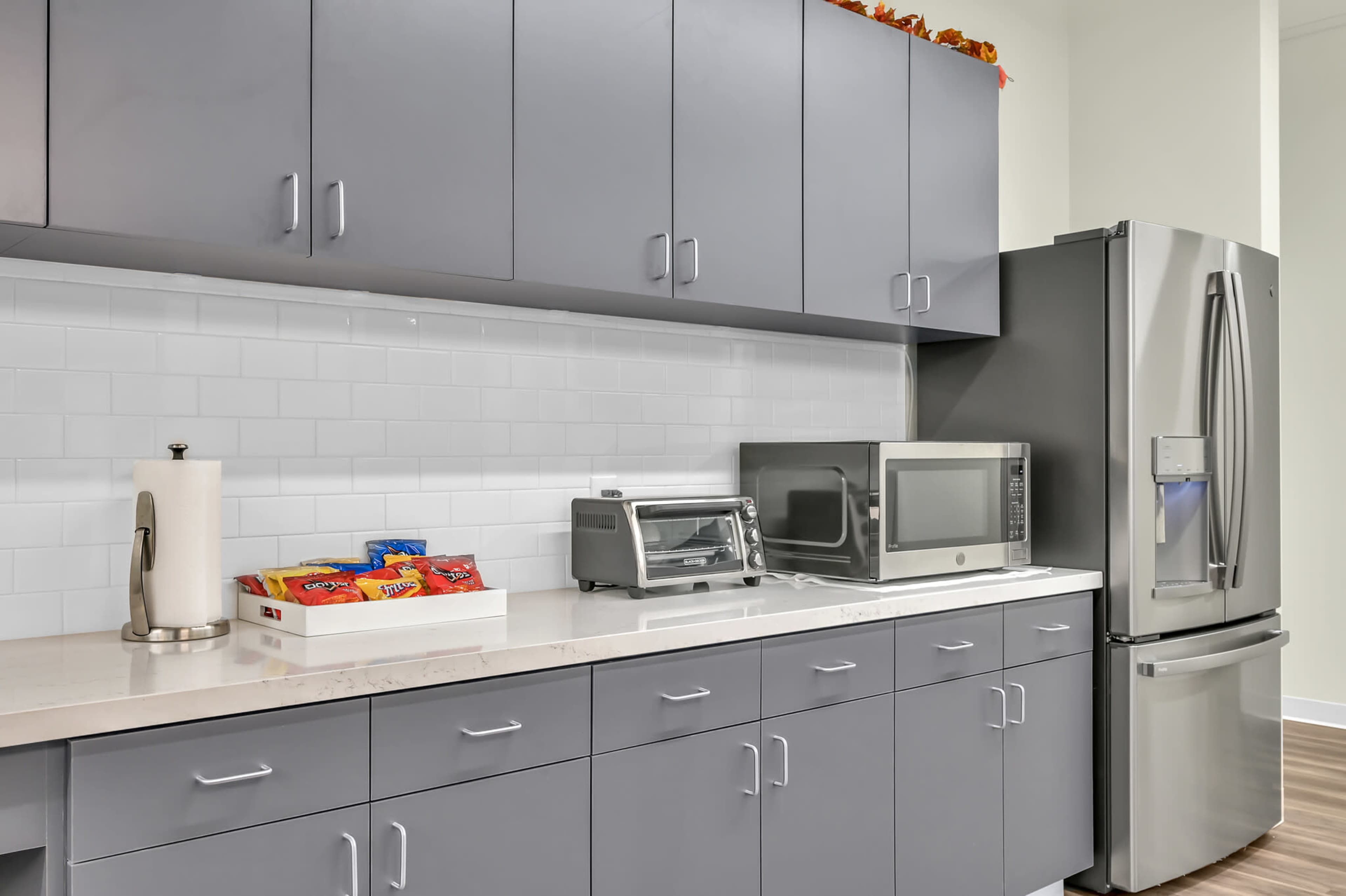A modern kitchen features gray cabinets, a stainless steel refrigerator, a microwave, and a countertop with a tray of snacks.