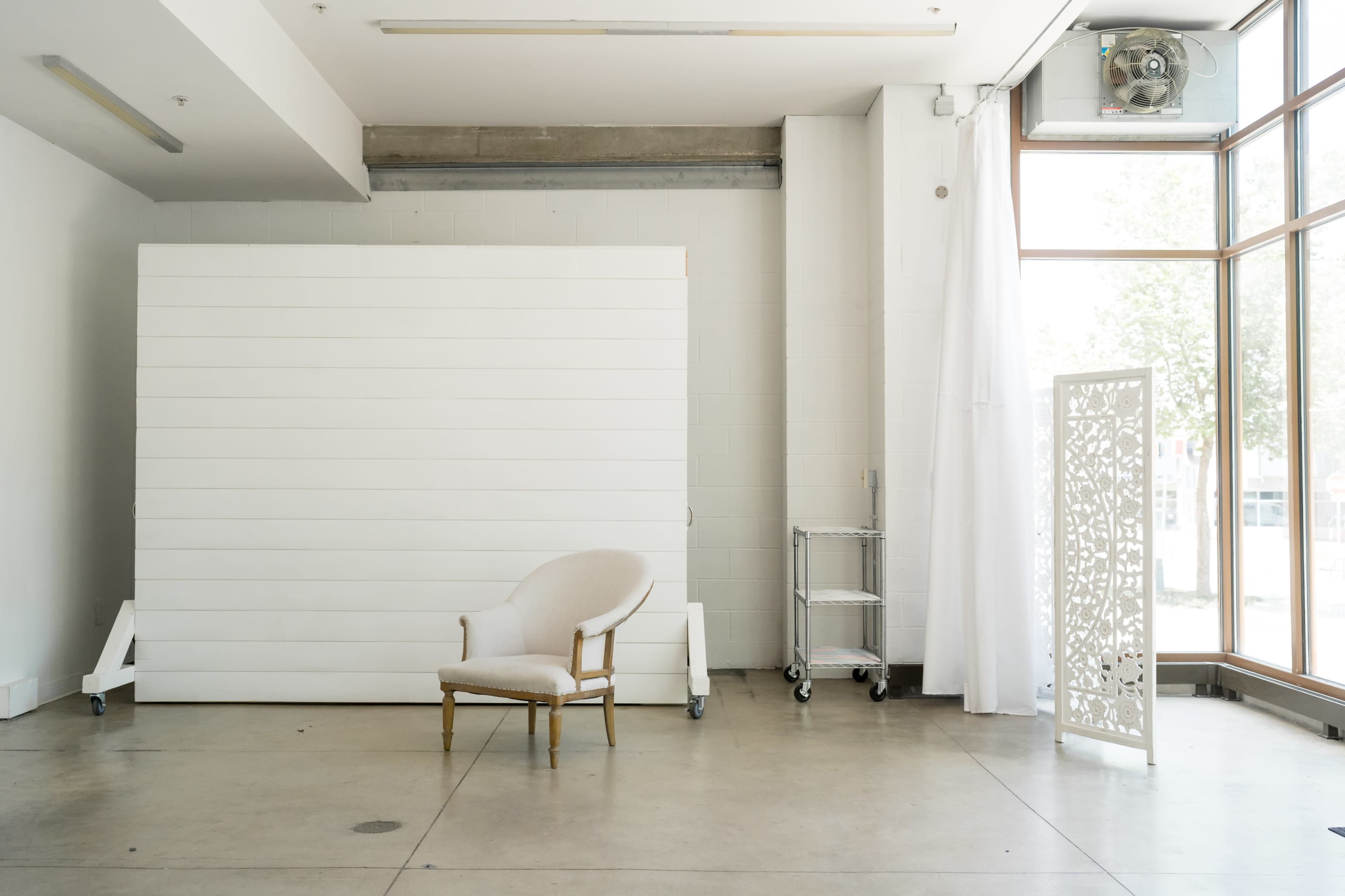 A minimalistic interior space with a white wooden backdrop, a single chair, and a decorative screen.