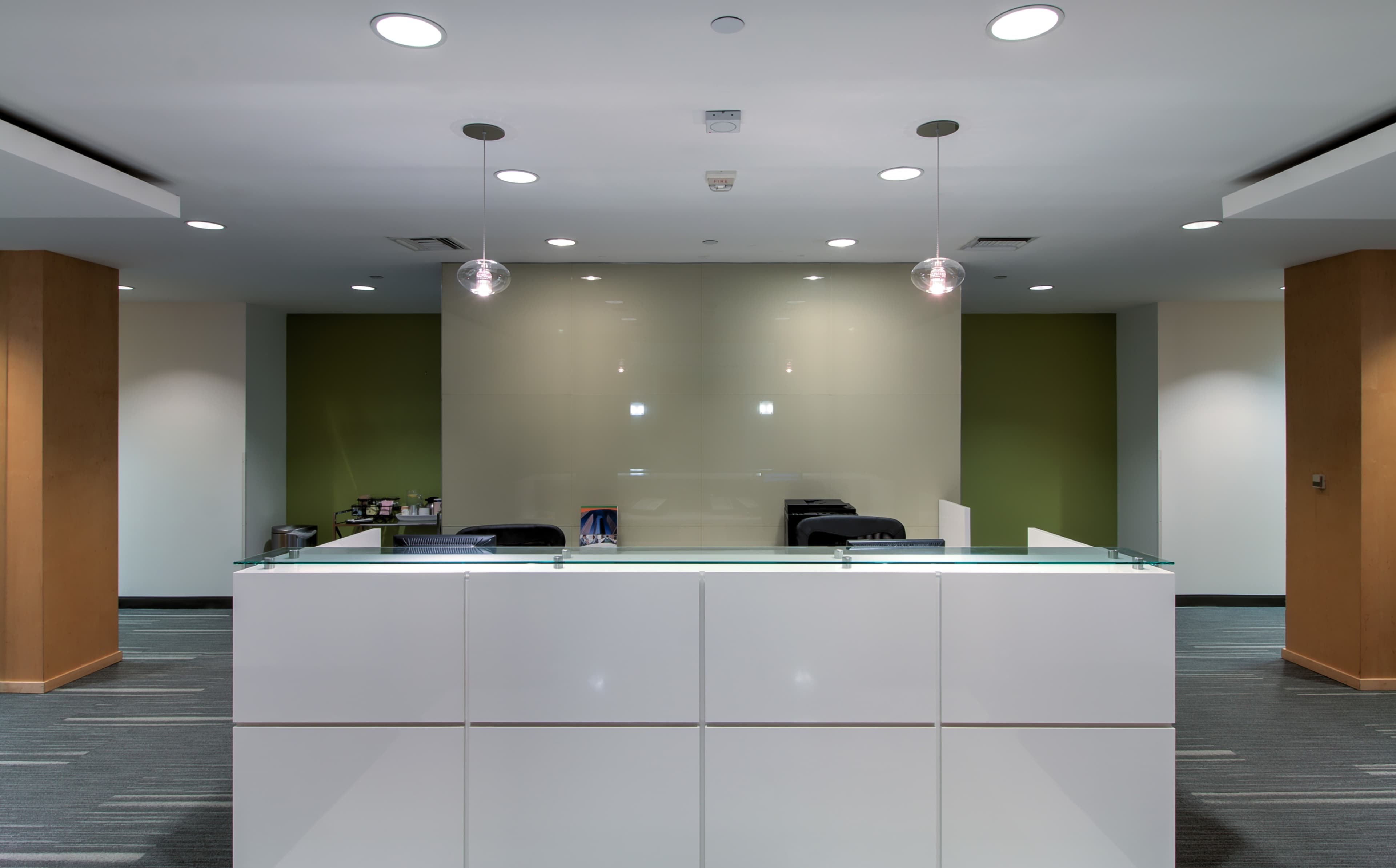 A modern reception area with a white front desk and green accent walls, illuminated by pendant lights.