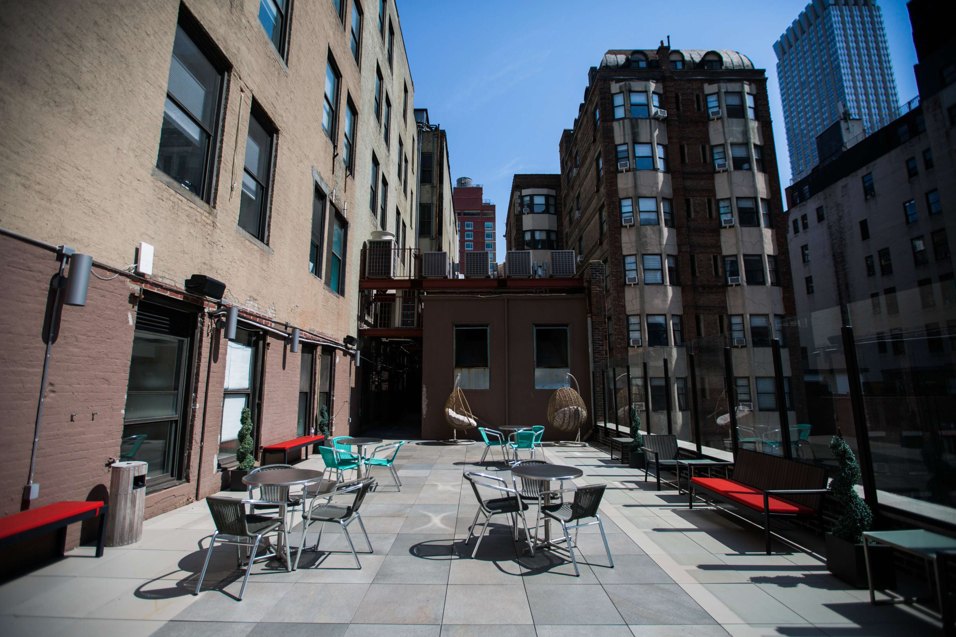 The image shows a rooftop patio featuring several tables and chairs, surrounded by buildings in an urban setting.