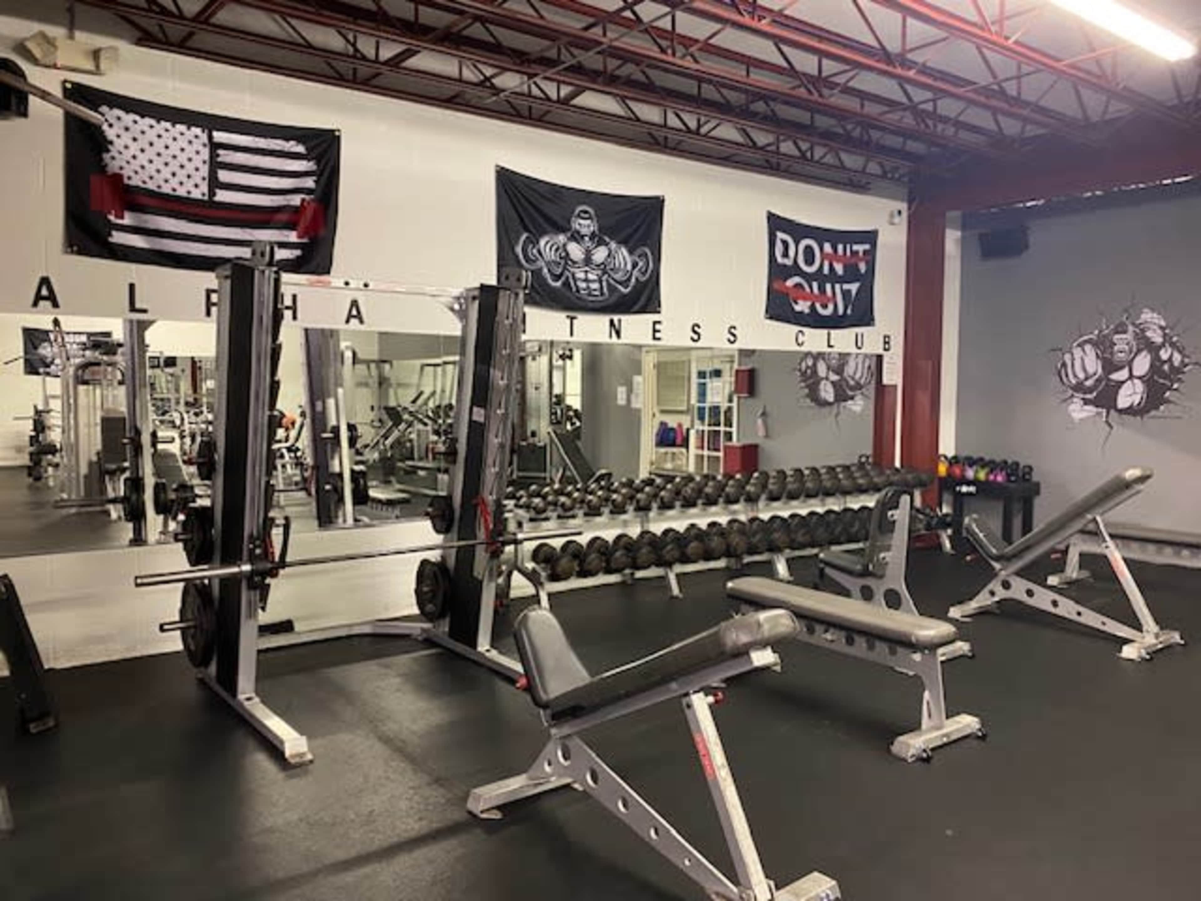The gym features a row of weightlifting benches, dumbbells, and motivational banners on the walls.