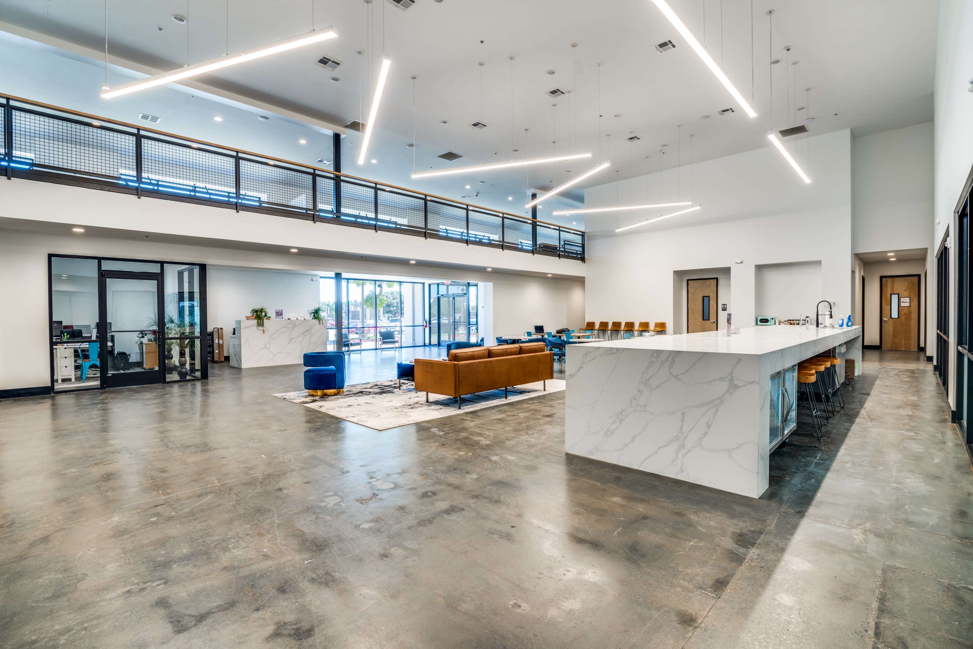 The image shows a spacious, modern interior with a large open area featuring a marble countertop, seating areas, and large windows allowing natural light in.