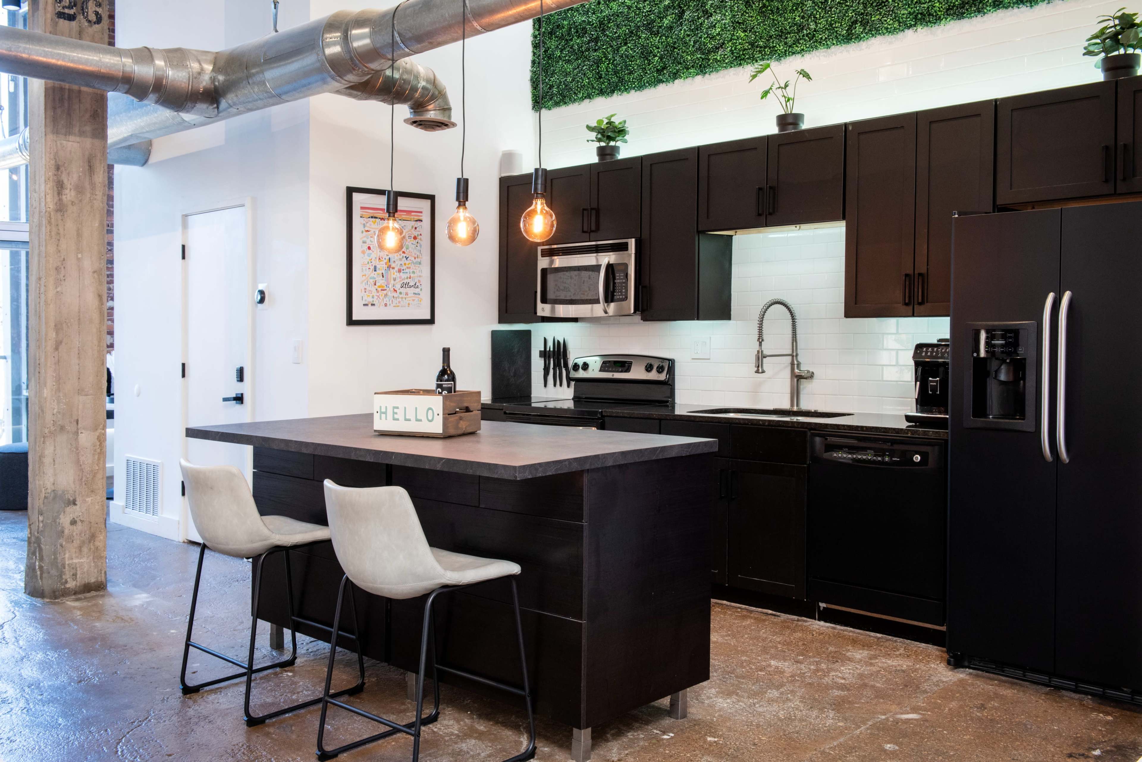 A modern kitchen featuring dark cabinetry, stainless steel appliances, a black island with seating, and decorative plants on the wall above.