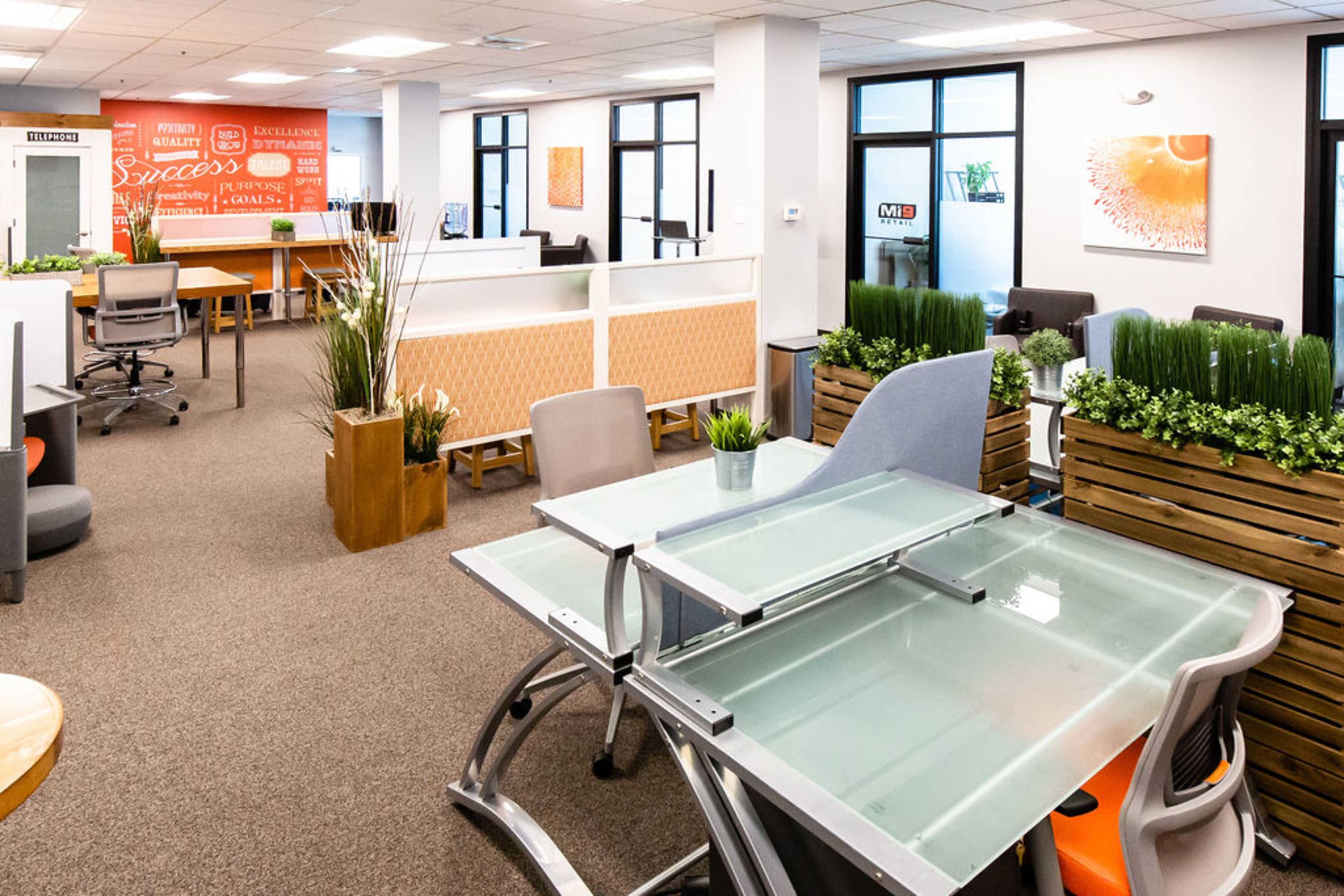 A modern office space with workstations, glass tables, and decorative plants.