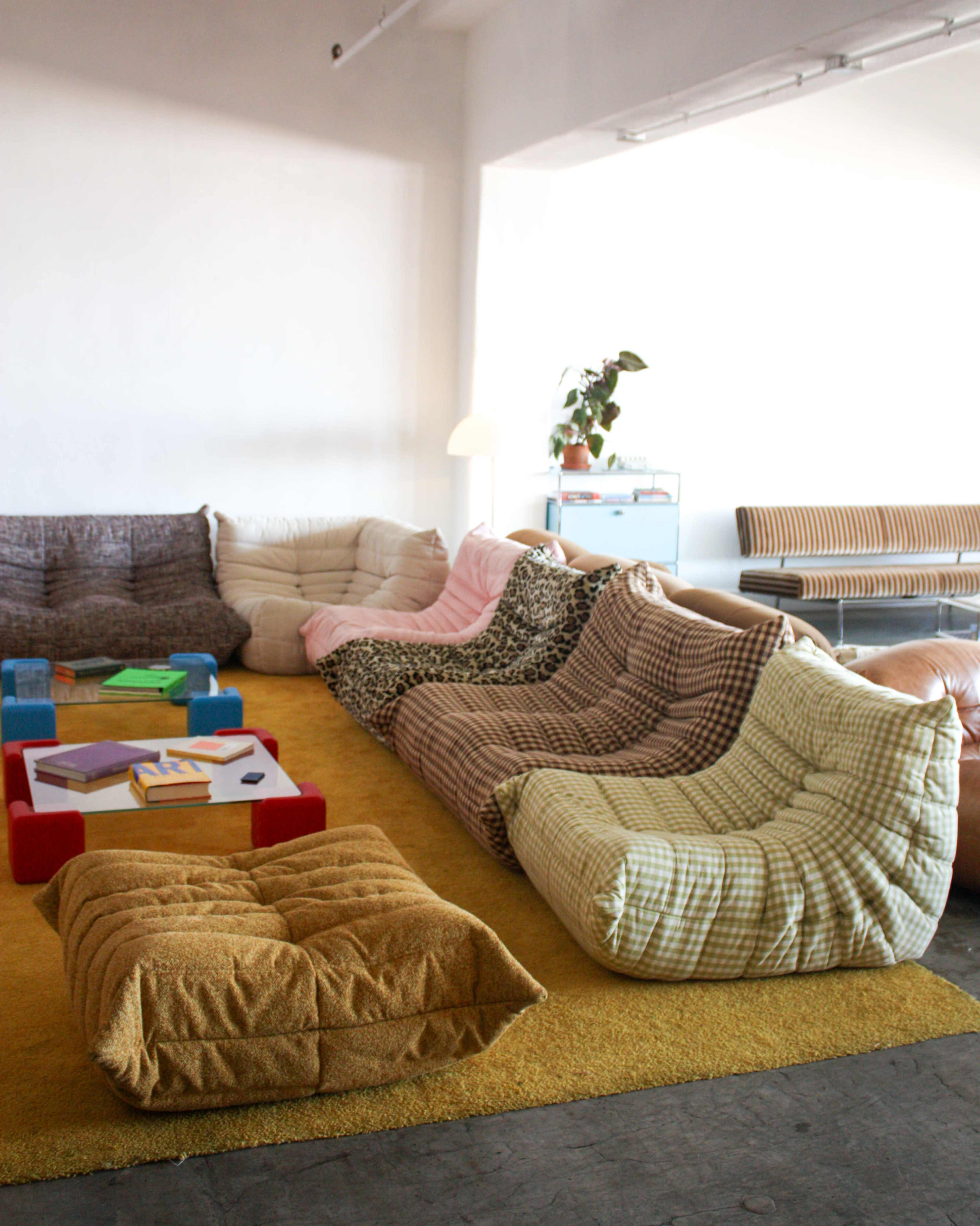 The image shows a spacious room filled with several large, cushioned lounge seats in various colors and patterns arranged over a textured yellow rug.