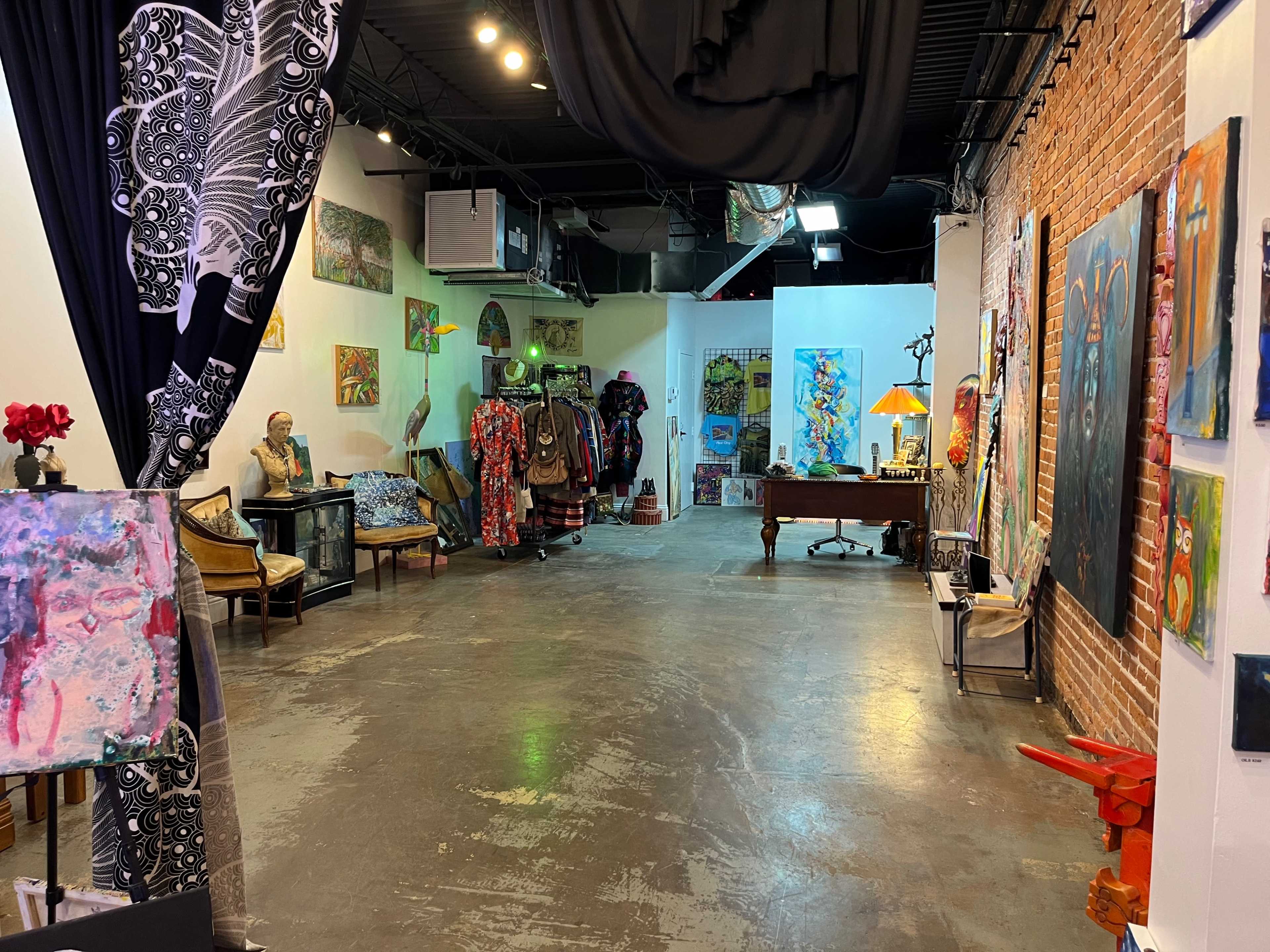 A spacious art gallery with exposed brick walls, various colorful paintings displayed, and decorative furniture arranged around the room.