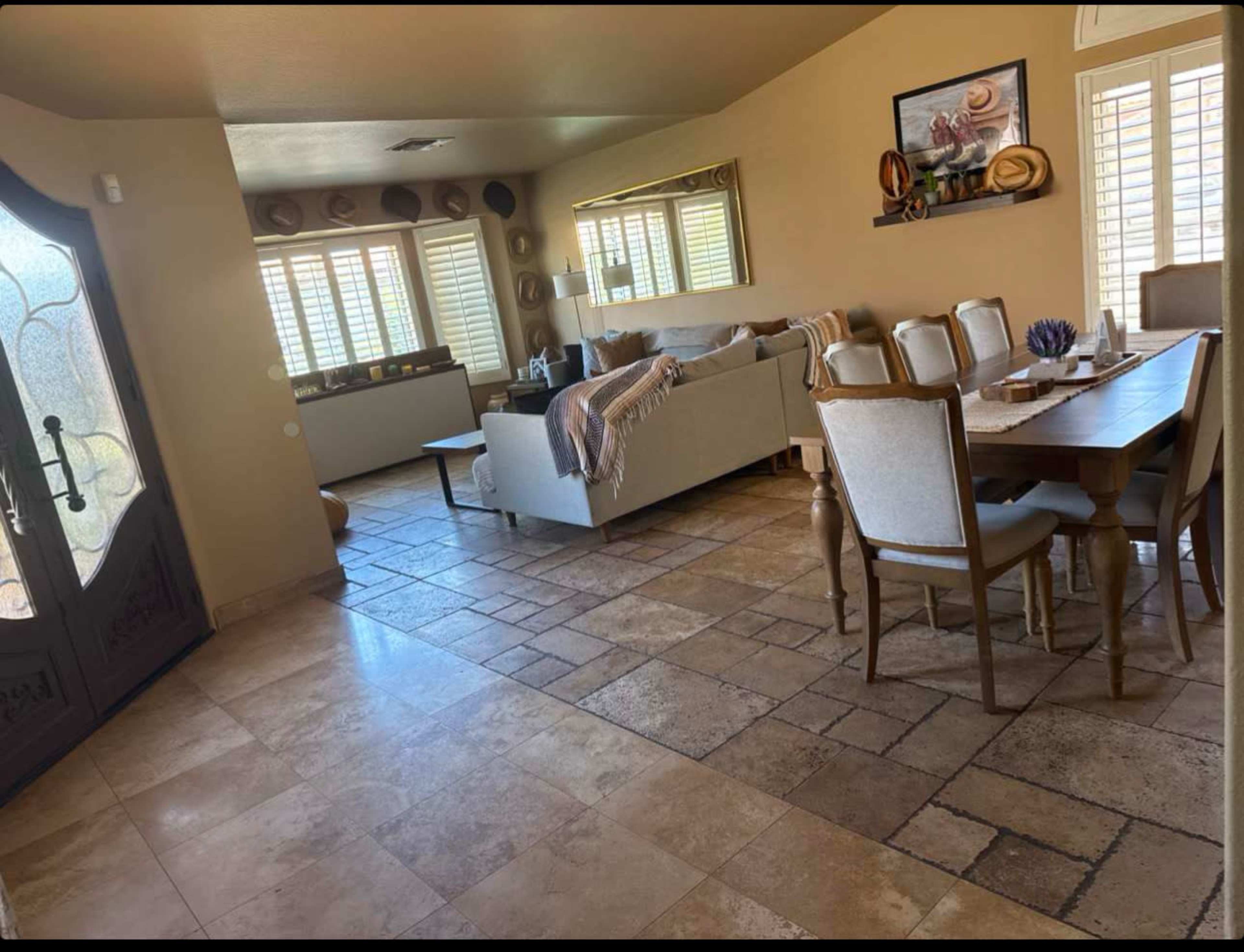 The image shows a spacious living area with a couch, dining table, and large windows that provide natural light.